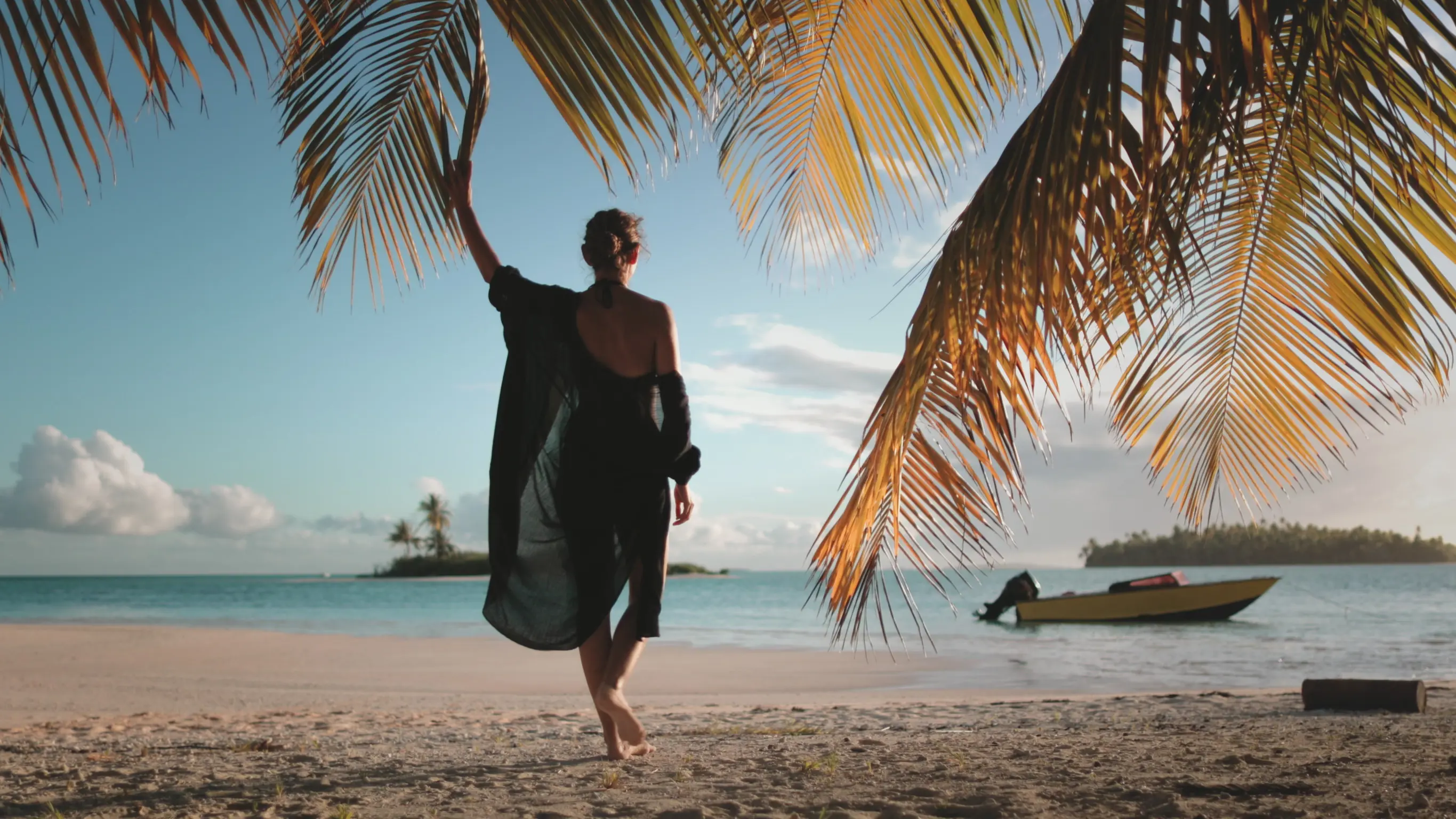 Kvinna i randig solhatt njuter av en solnedgång vid infinitypoolen med utsikt över havet och en palm.