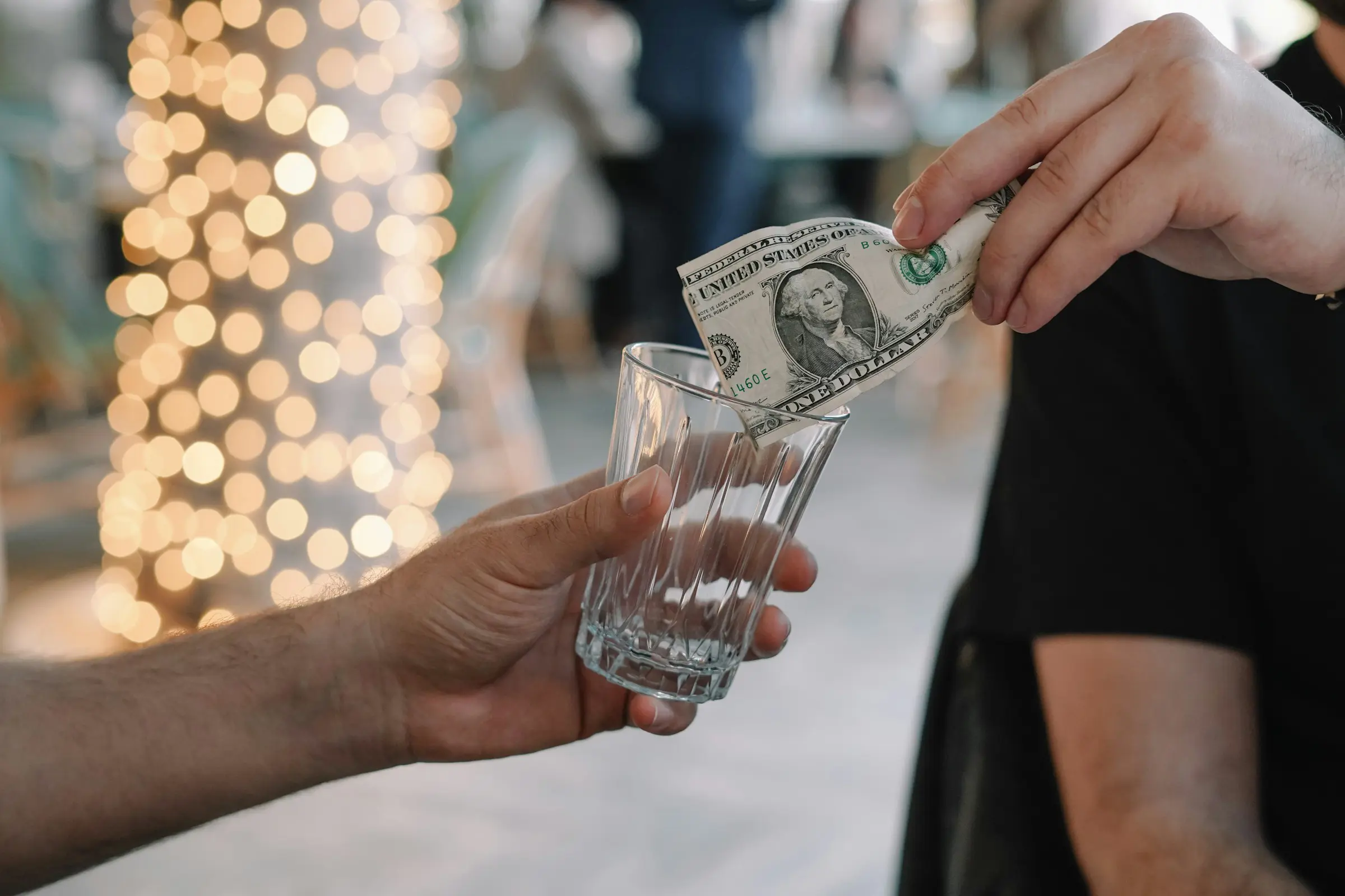 Person lämnar dricks genom att lägga en dollarsedel i ett glas med suddig bakgrund.
