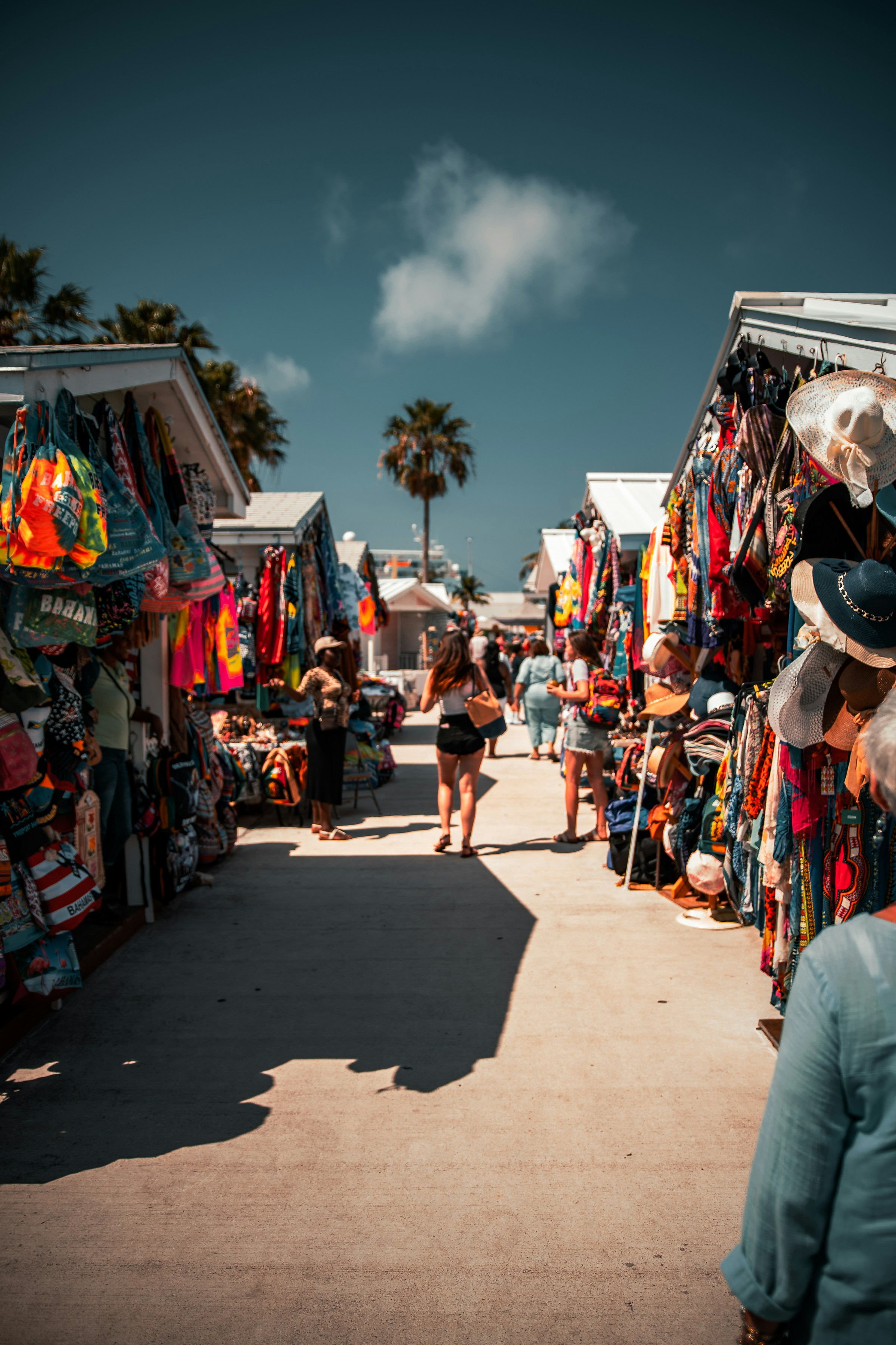 Travellers visiting a colourful local market with clothes, hats and souvenirs during a sunny holiday.