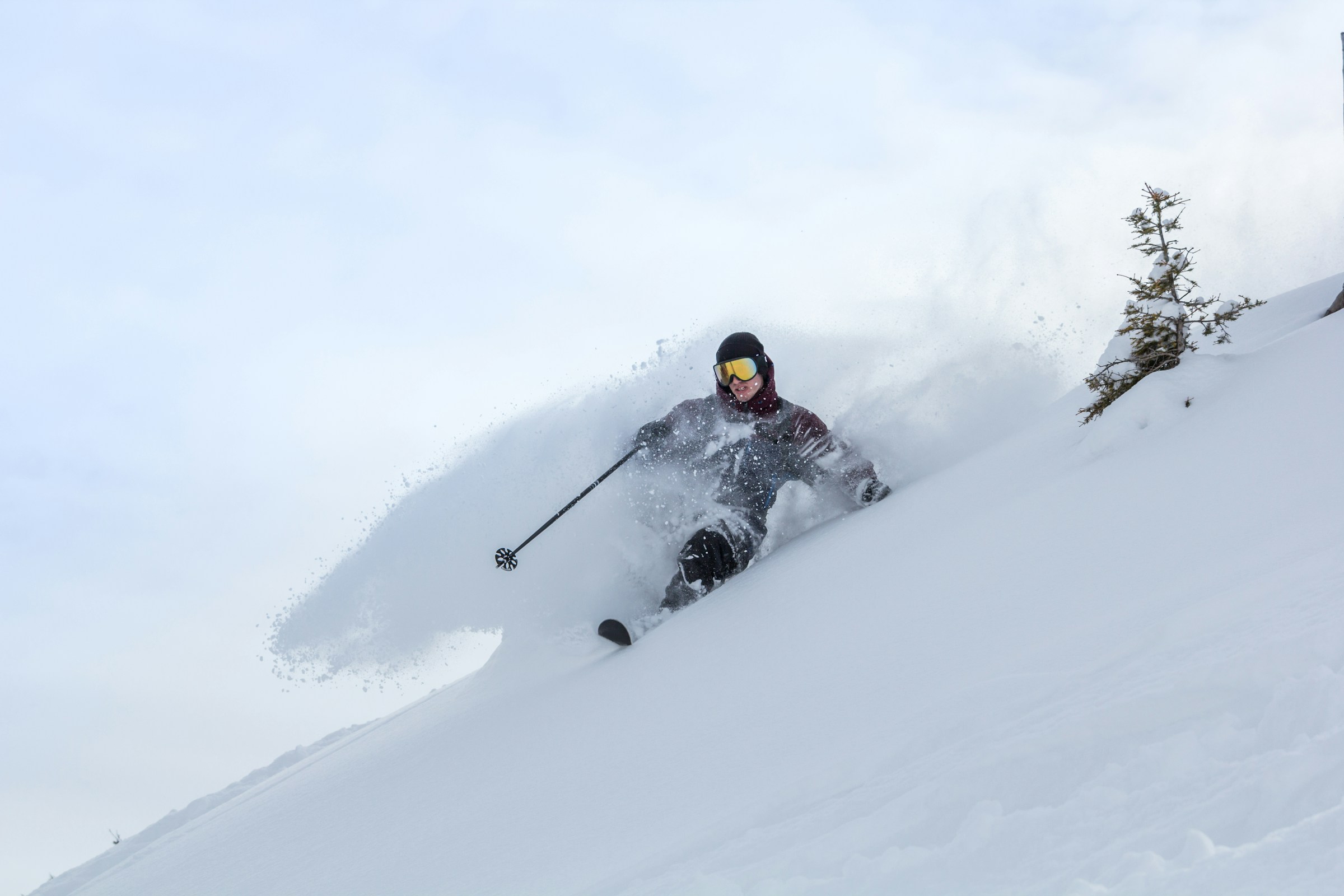 Man skiing down a snow-covered slope with snow flying around him with blue sky in the background