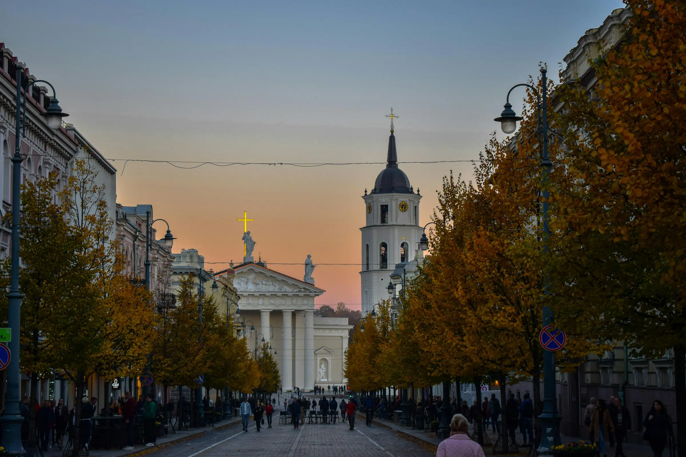 Street view of Vilnius Cathedral at sunset, featuring autumn trees lining the path and a clear sky above the historic architecture in Lithuania