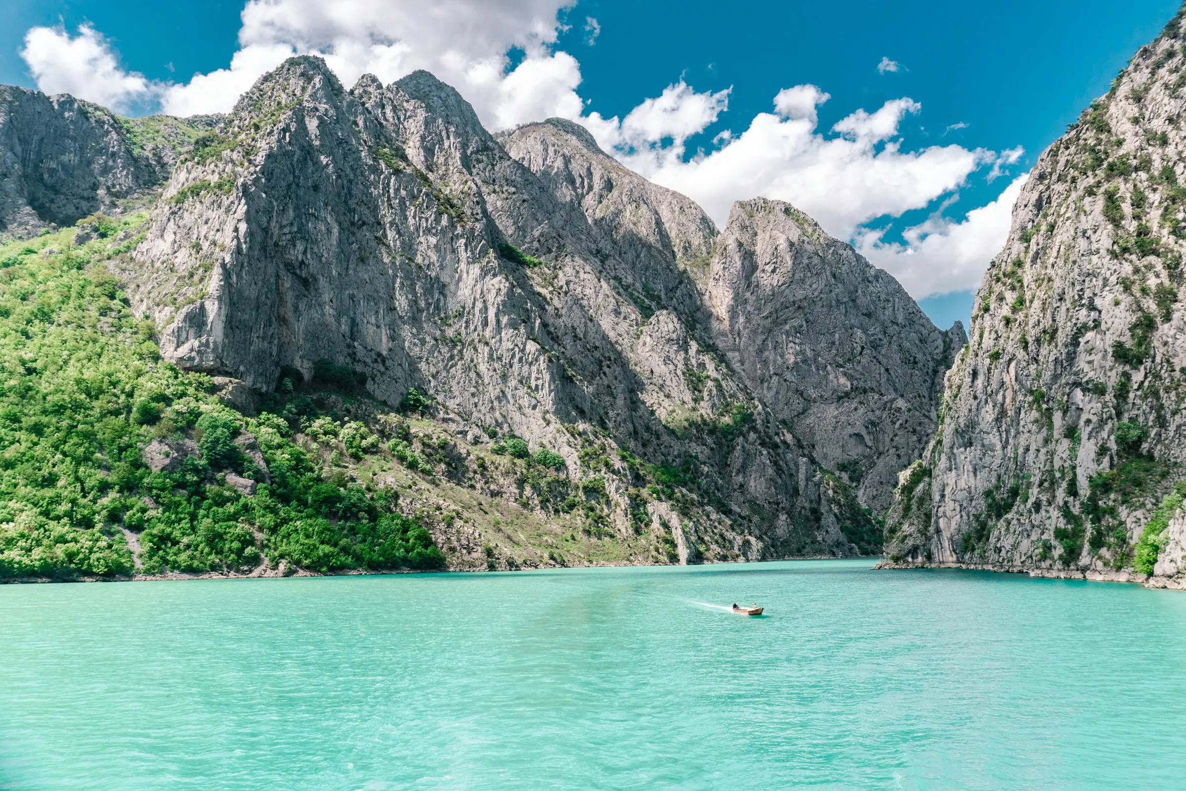 Turquoise waters and a small boat surrounded by lush green mountains and rocky cliffs in Albania.