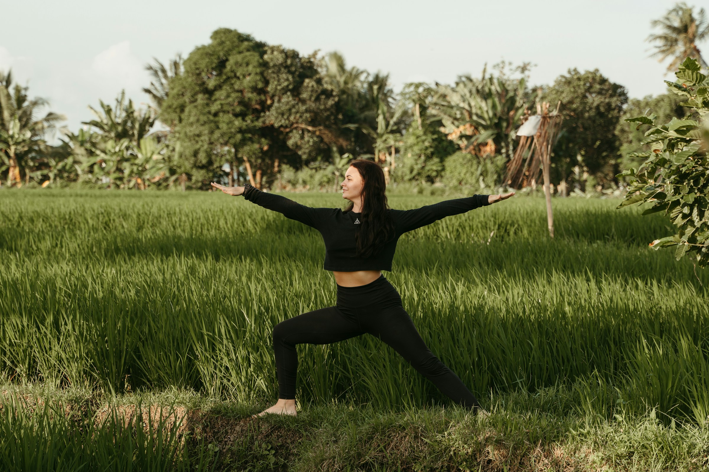 kvinna klädd i svart övar yoga på sin träningsresa i naturen på bali
