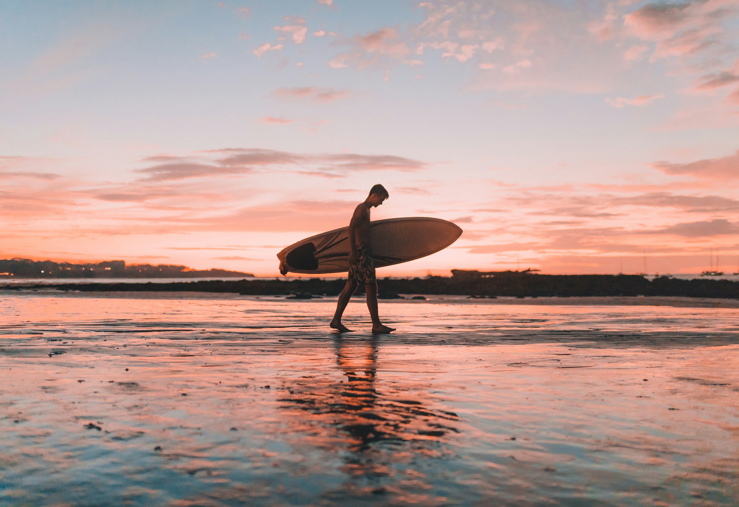 Man bär på surfbräda i solnedgång på stranden i Costa Rica under sin träningsresa