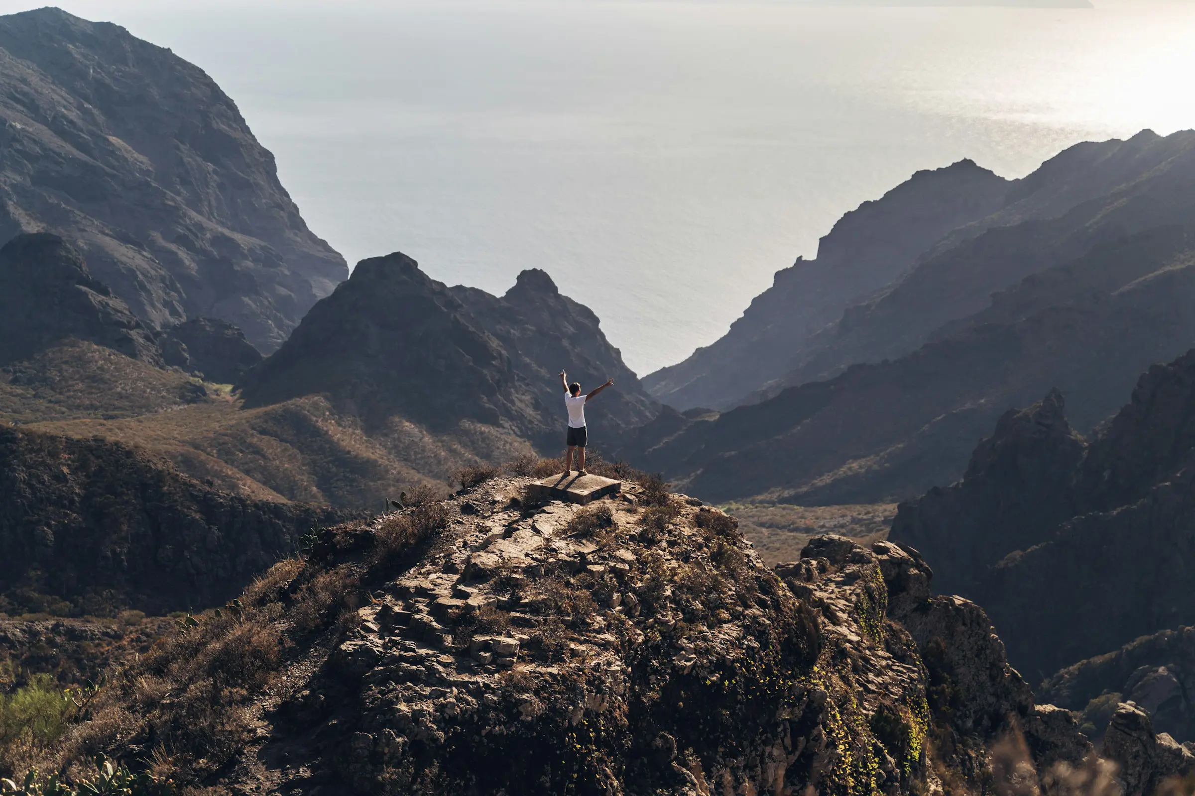 man standing on a cliff and looking at nature and mountains at sunset in Tenerife