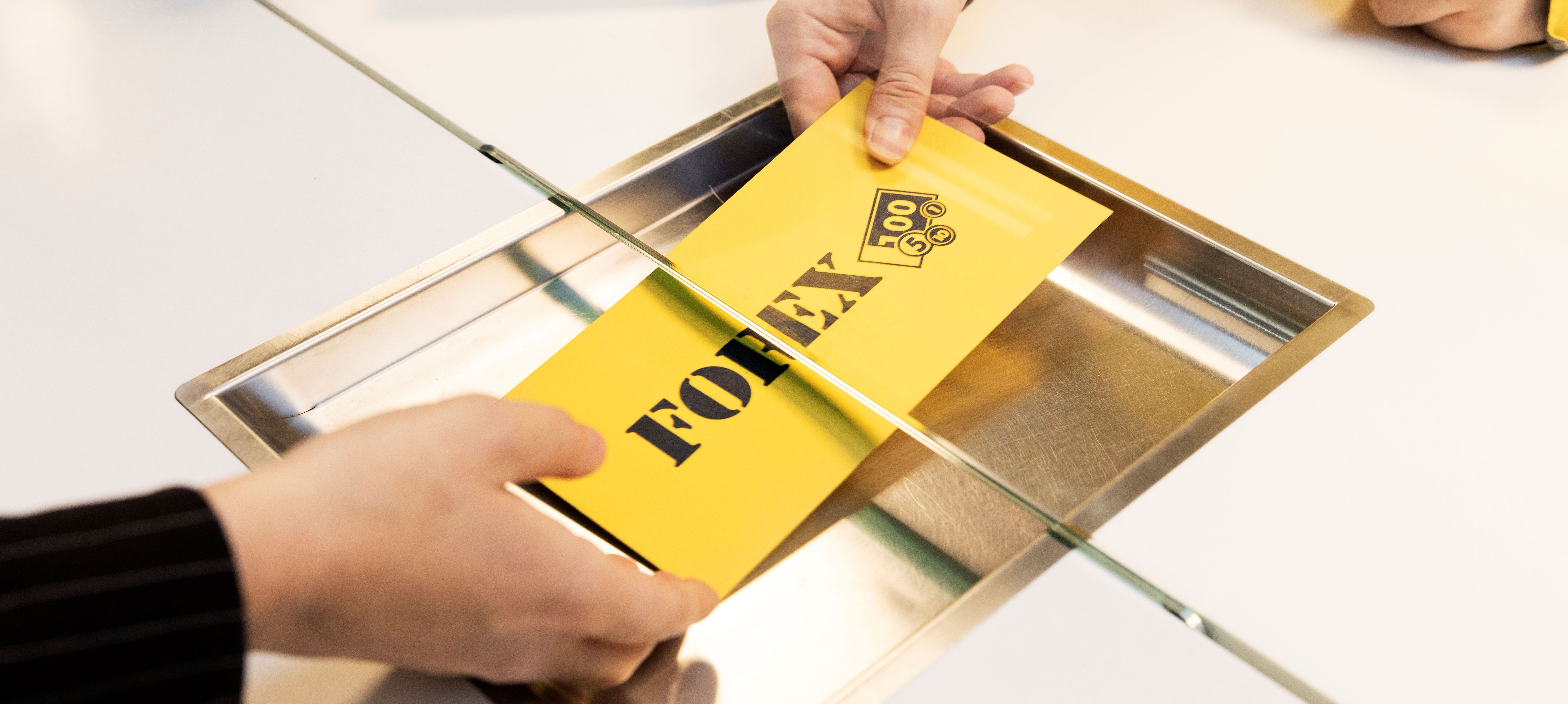 Person överlämnar ett gult Forex-kuvert genom en servicelucka.
