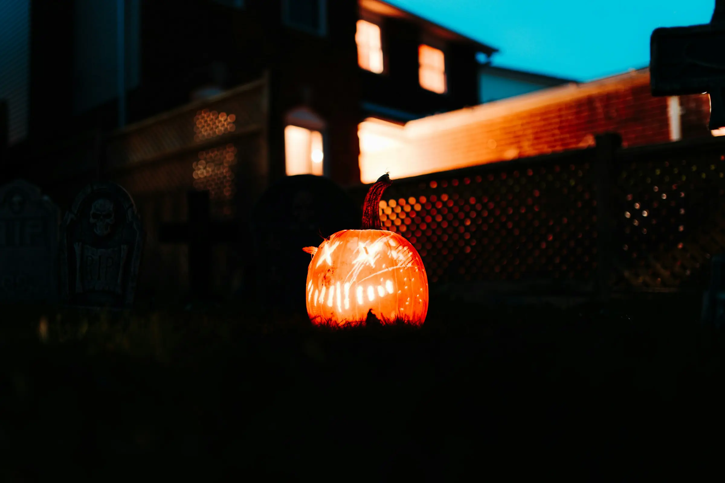 Lysande uthålad pumpa med Halloween-snittmönster i skymningen framför hus och staket.