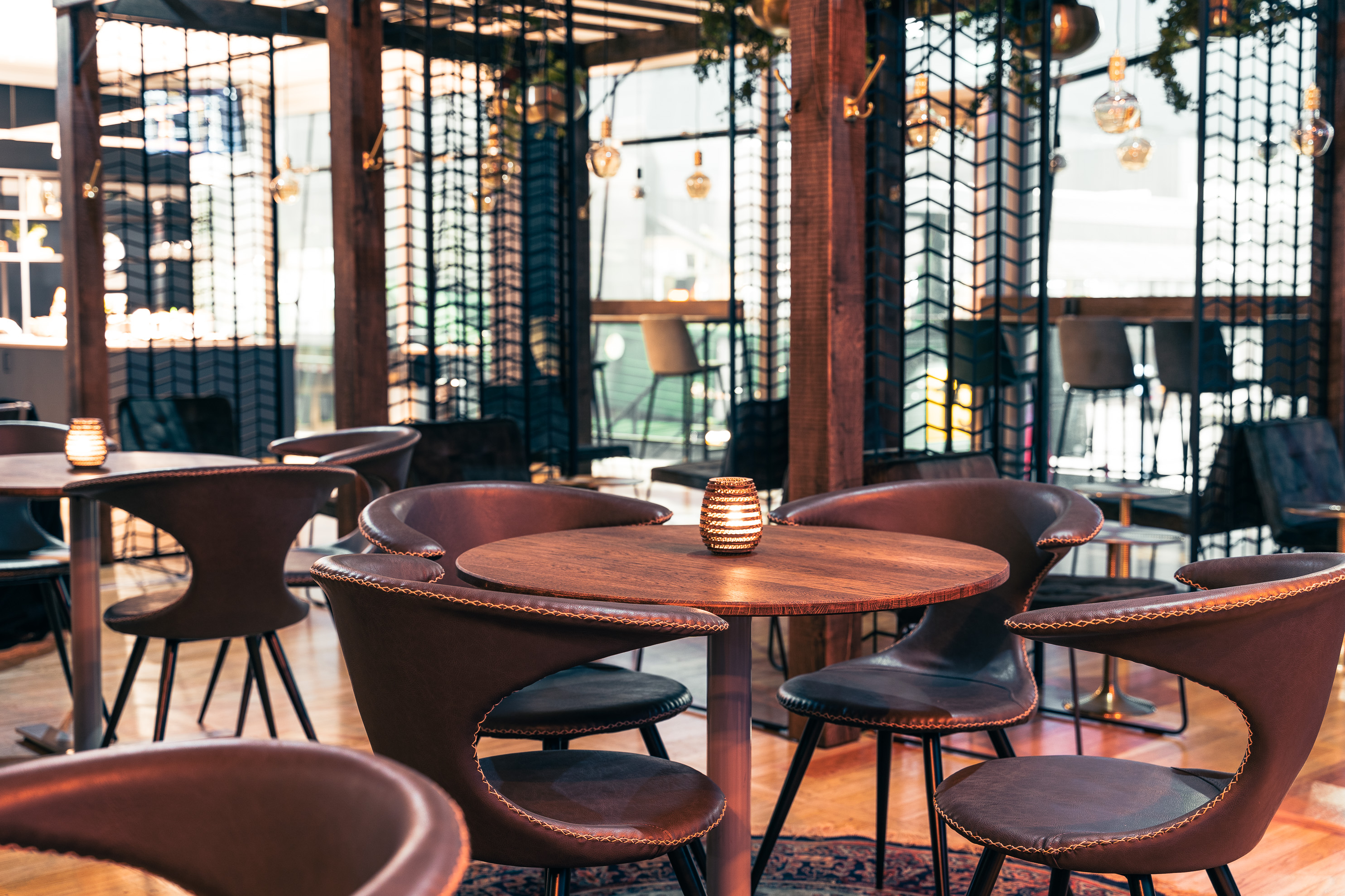 Modern restaurang med stilren inredning, atmosfärisk belysning och eleganta mörka träbord omgivna av designstolar.