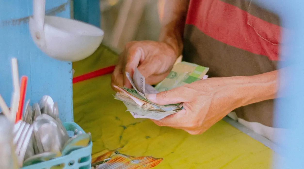 Person r&auml;knar en bunt sedlar vid en disk, med skedar och k&ouml;ksredskap i en beh&aring;llare bredvid.