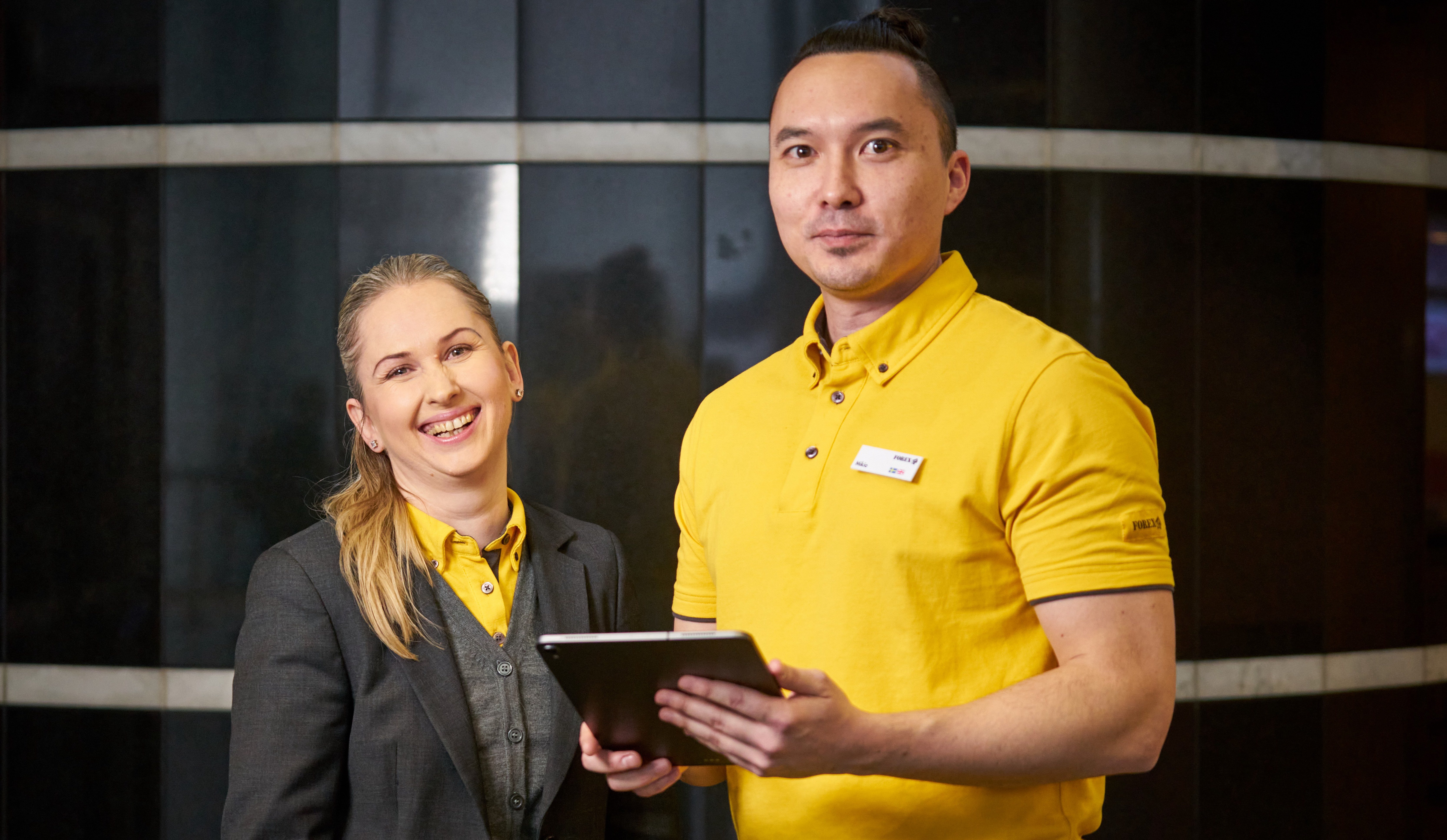 FOREX employees in a currency exchange store with a tablet, wearing FOREX work uniforms.