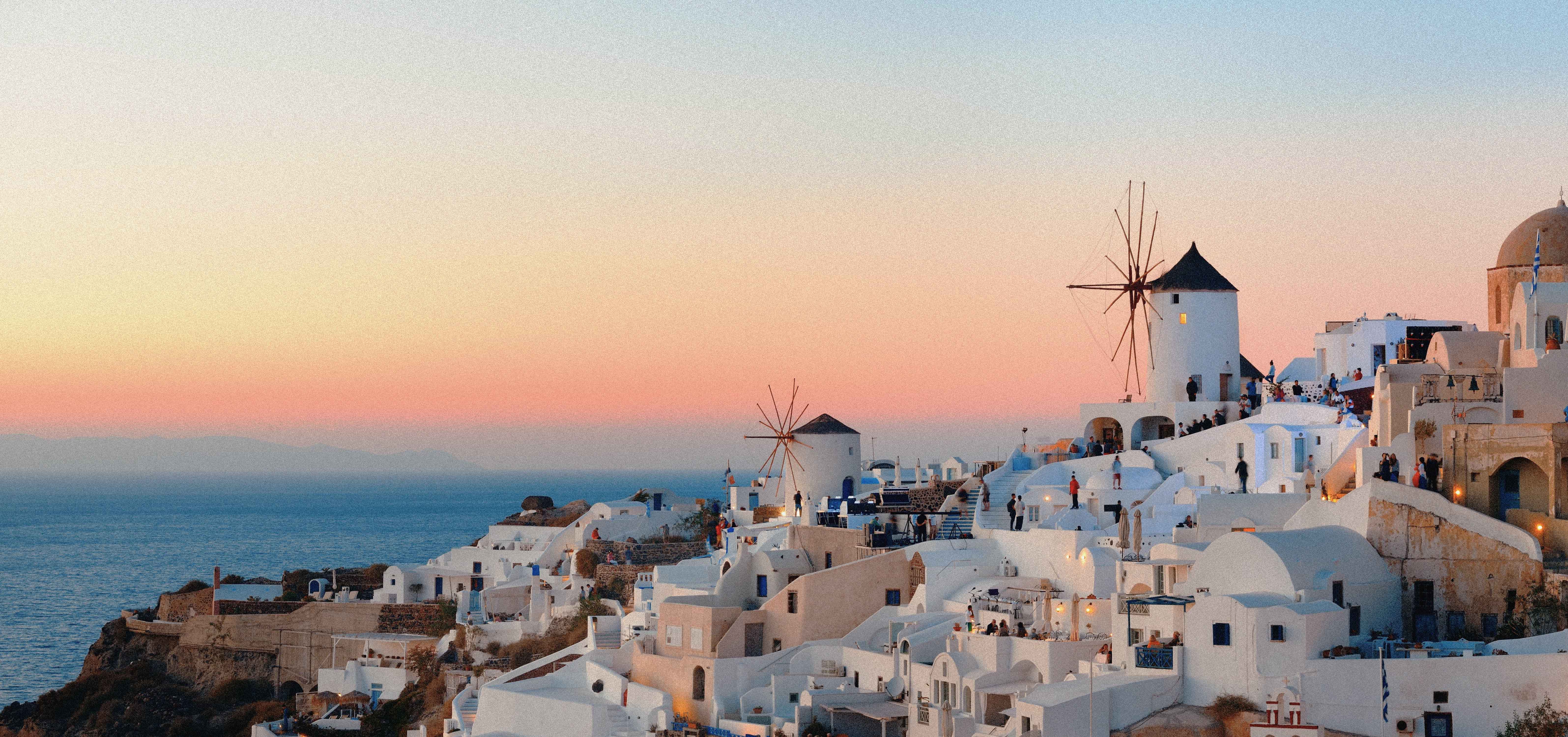 Vitkalkade hus och klassiska väderkvarnar i Oia på Santorini under solnedgång. Romantisk utsikt över Egeiska havet i Grekland.