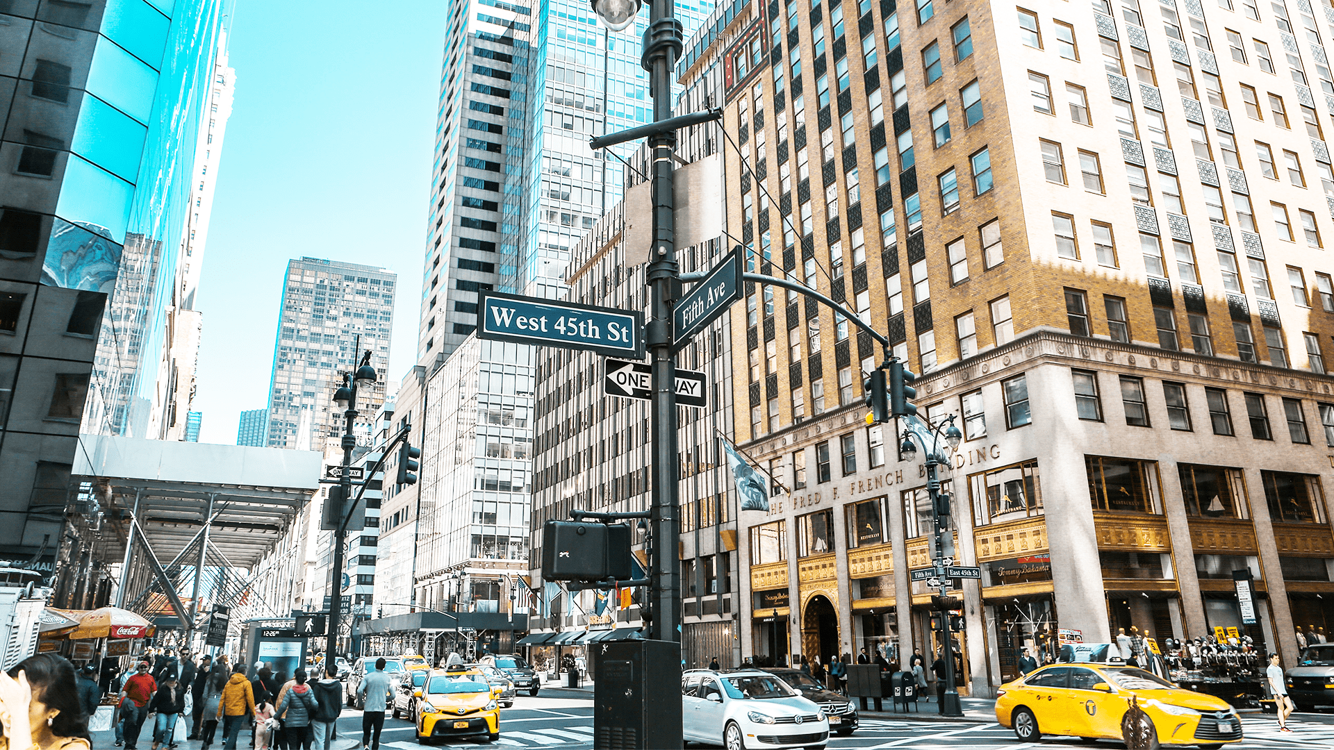 Bustling New York City street scene at the intersection of West 45th Street and Fifth Avenue, featuring tall buildings, pedestrians, and yellow taxis.