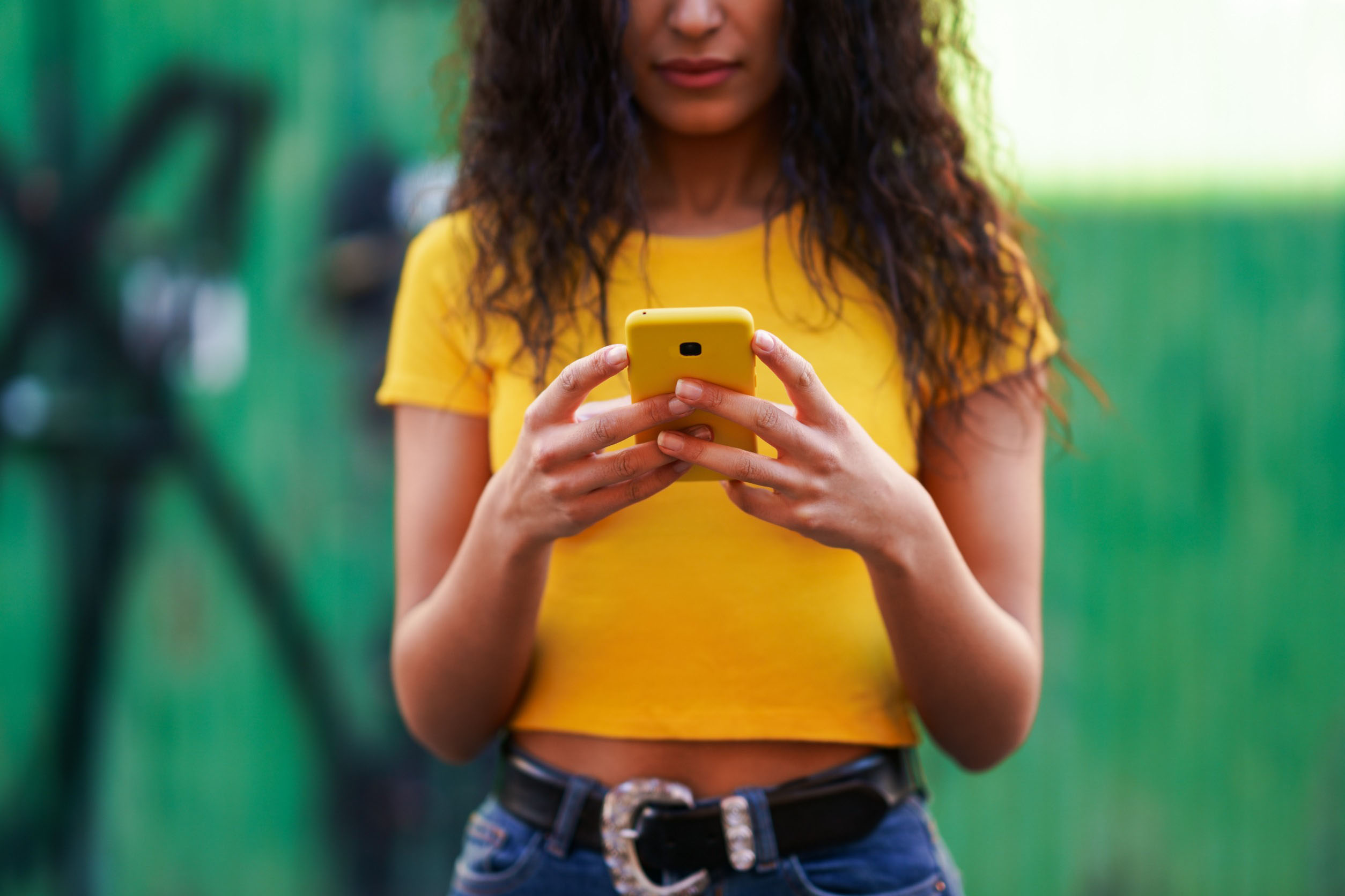 Woman in yellow top uses a yellow smartphone outdoors while checking her credit card insurance.