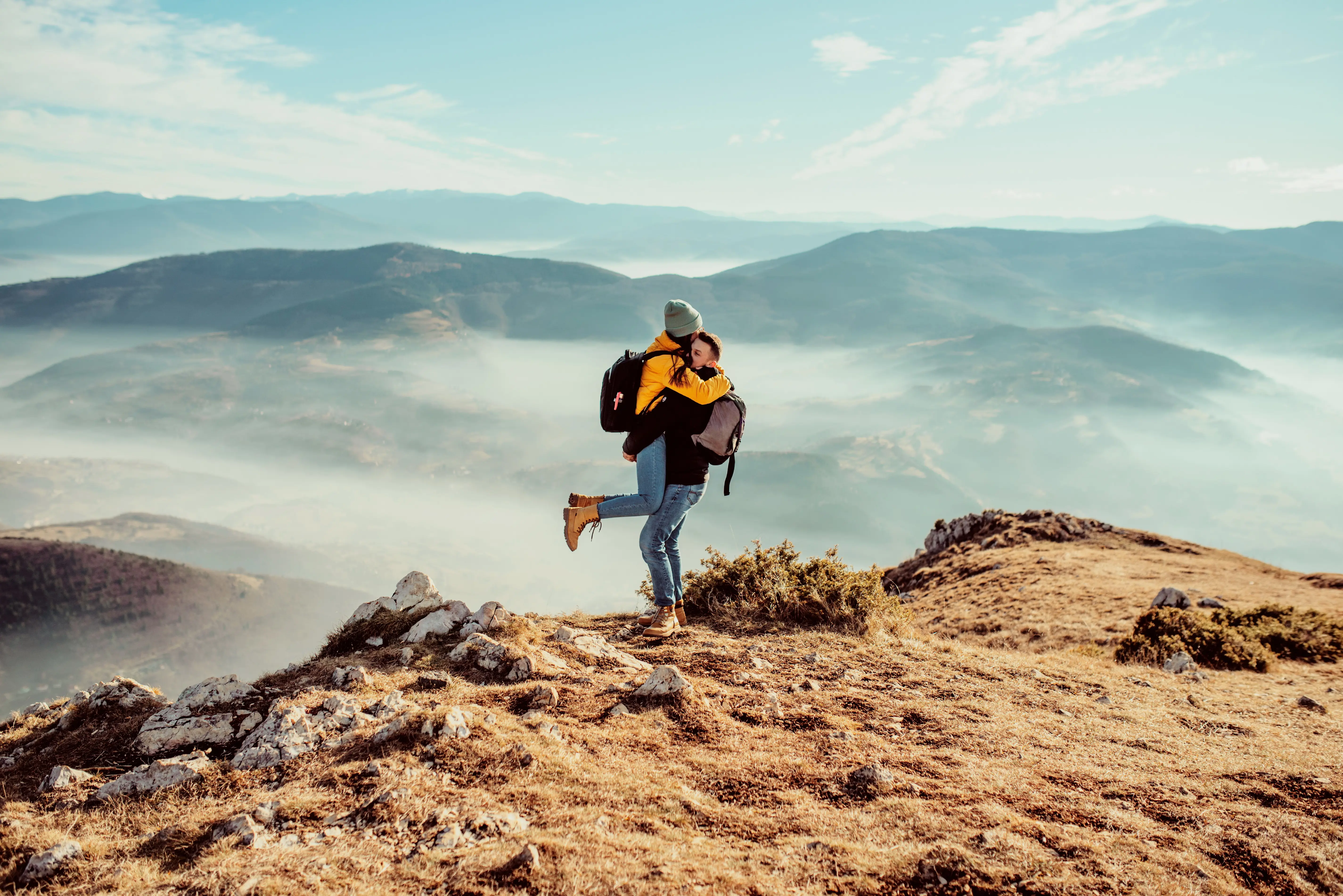 Couples embrace each other on a mountaintop with misty valleys in the background.