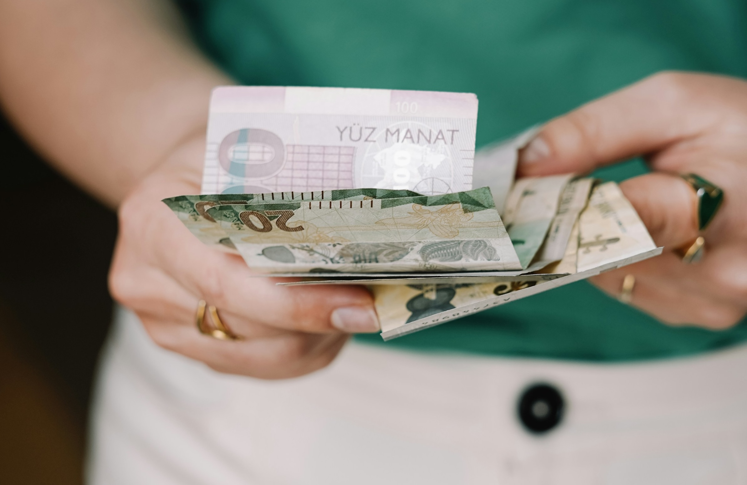 Personen håller turkmenistanmanater i handen, flera sedlar i ett knippe.
