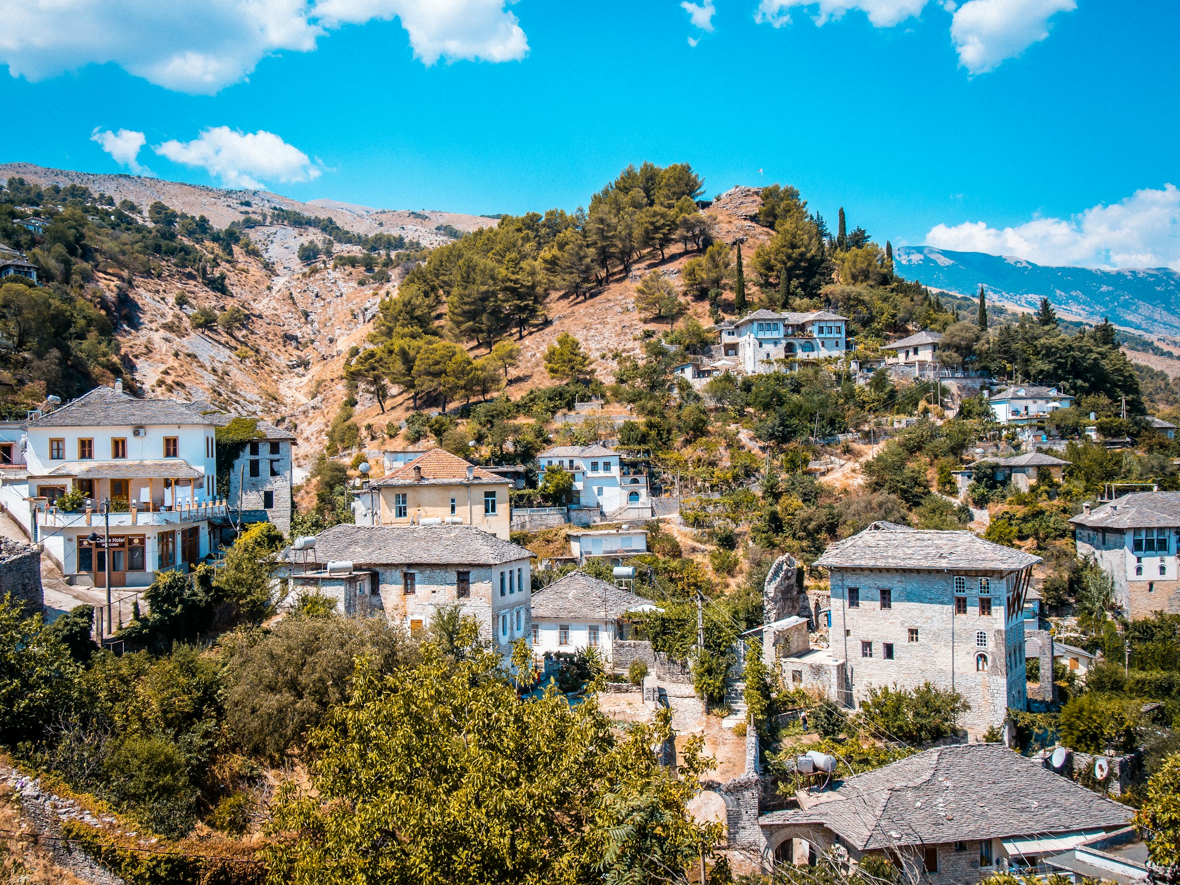 Scenic view of a traditional hillside village in Albania with stone houses and lush greenery under a bright blue sky.