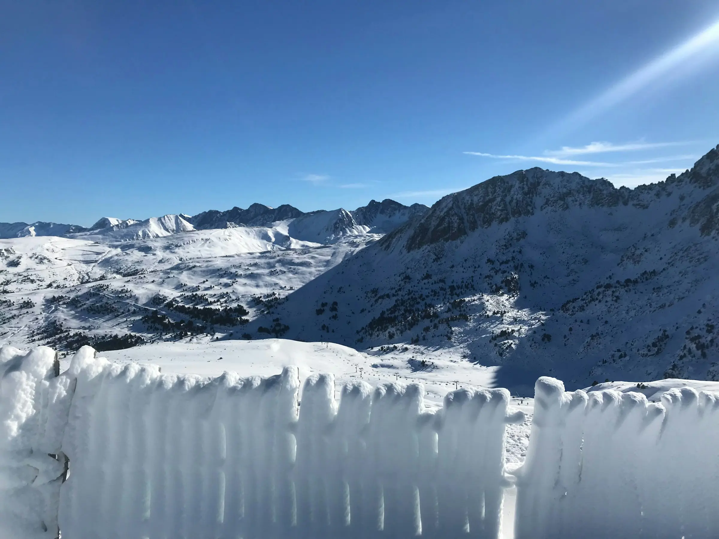 Snötäckt vinterlandskap som leder upp mot mäktiga berg och blå himmel i Grandvalira, Andorra