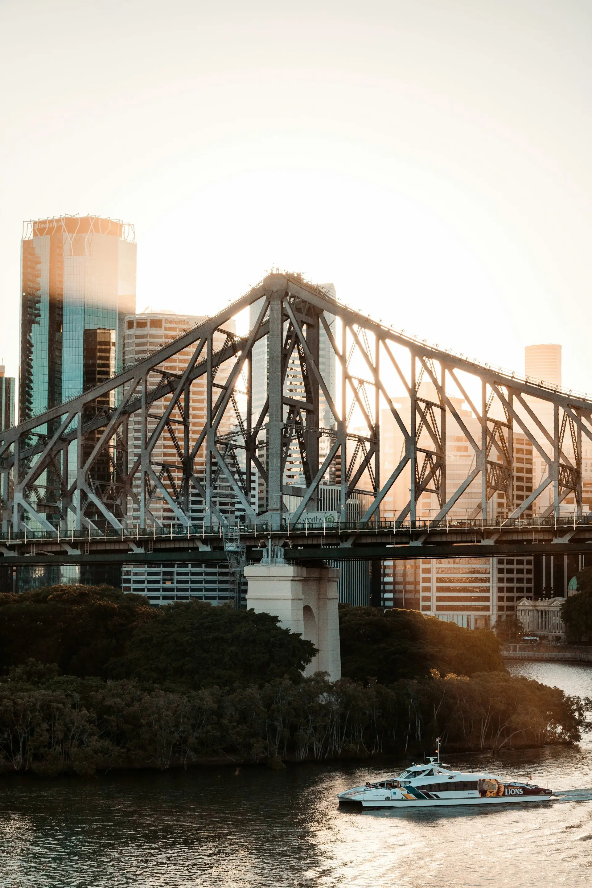 Iconic Story Bridge in Brisbane at sunset with a ferry on the Brisbane River, framed by city skyscrapers in the background.