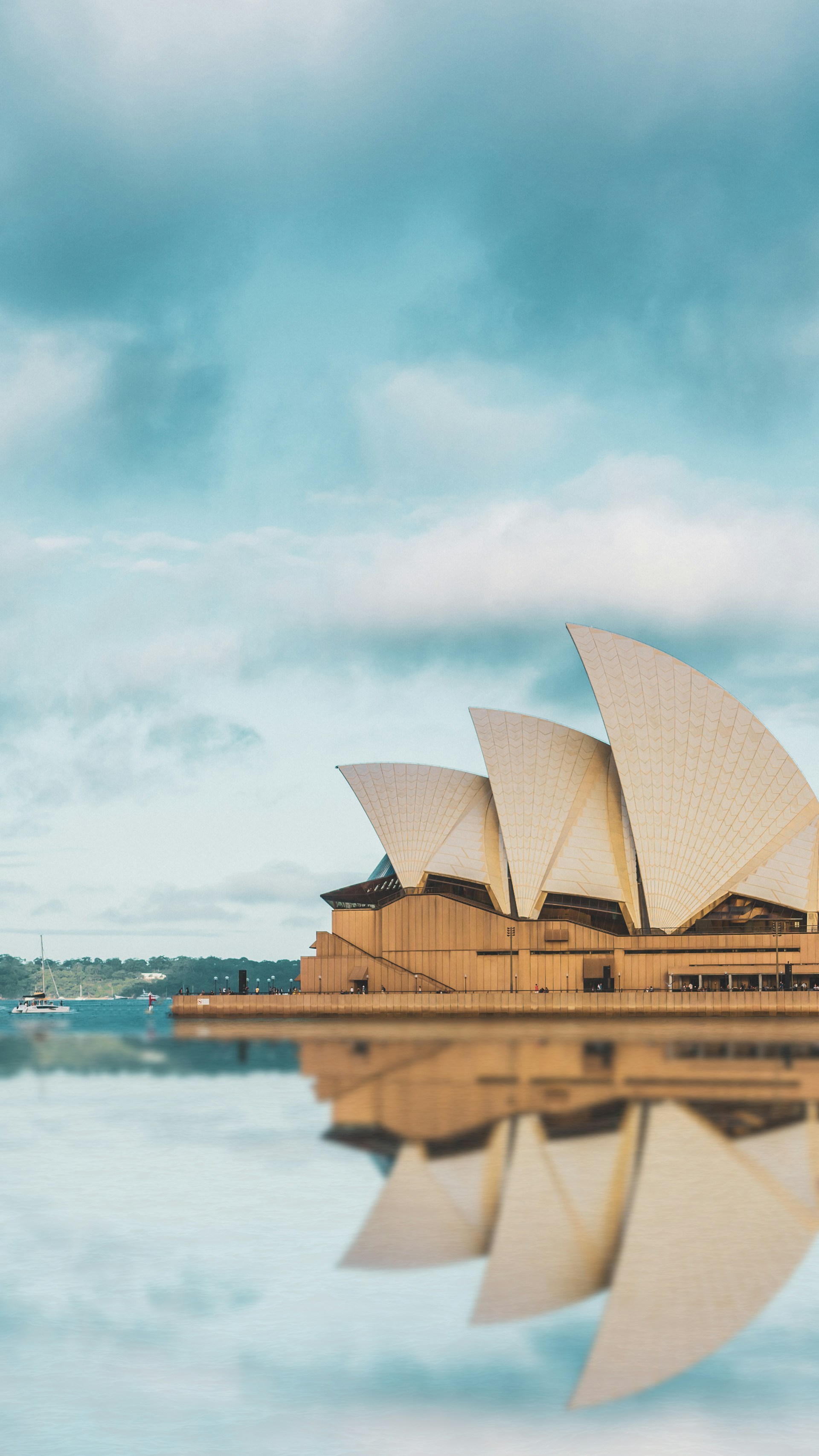 Sydney Opera House vid vatten med reflektion och blå himmel i bakgrunden, känd arkitektonisk landmärke i Australien.