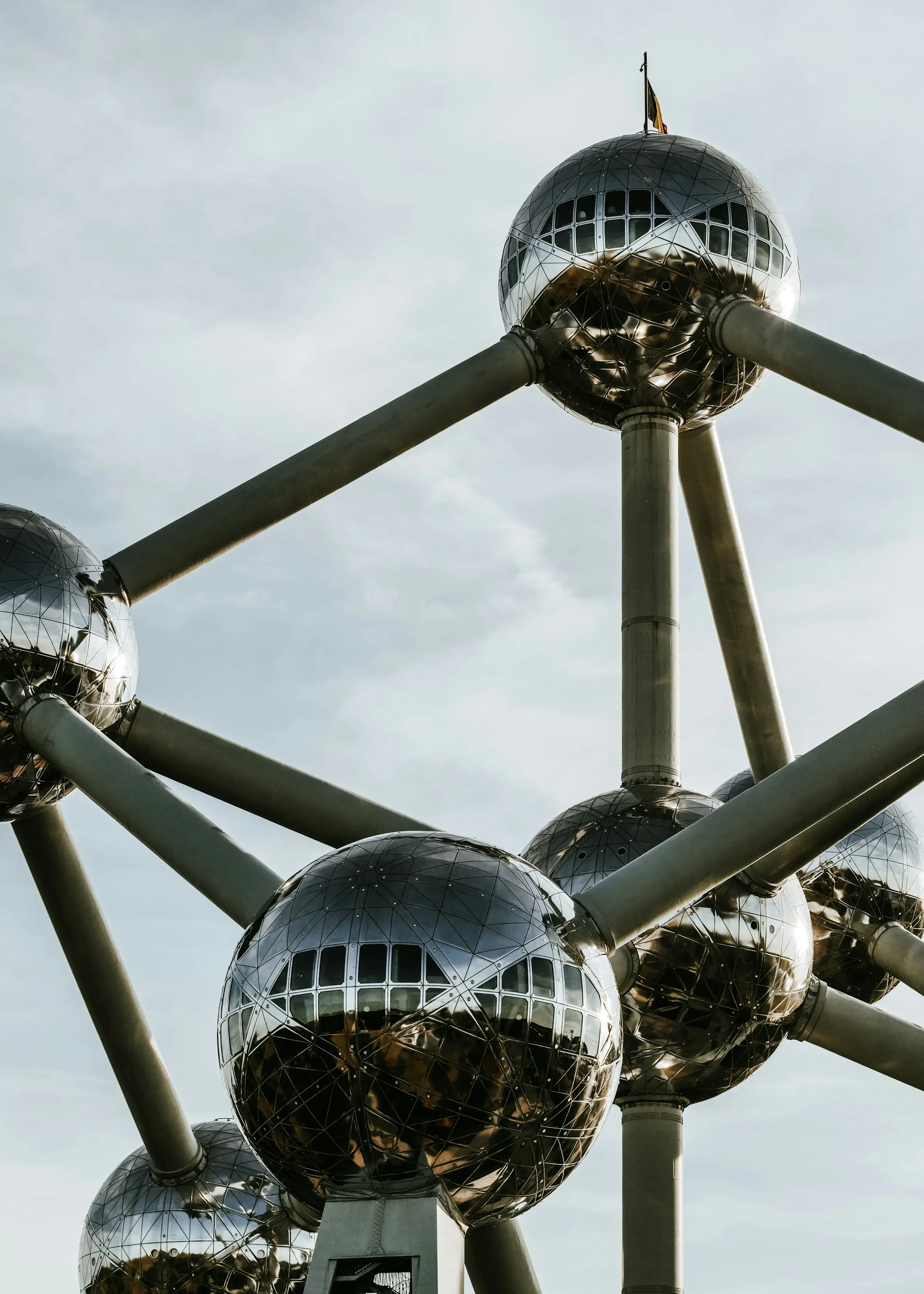 Close-up of the Atomium in Brussels, showcasing its metallic spheres and connecting tubes against a cloudy sky.