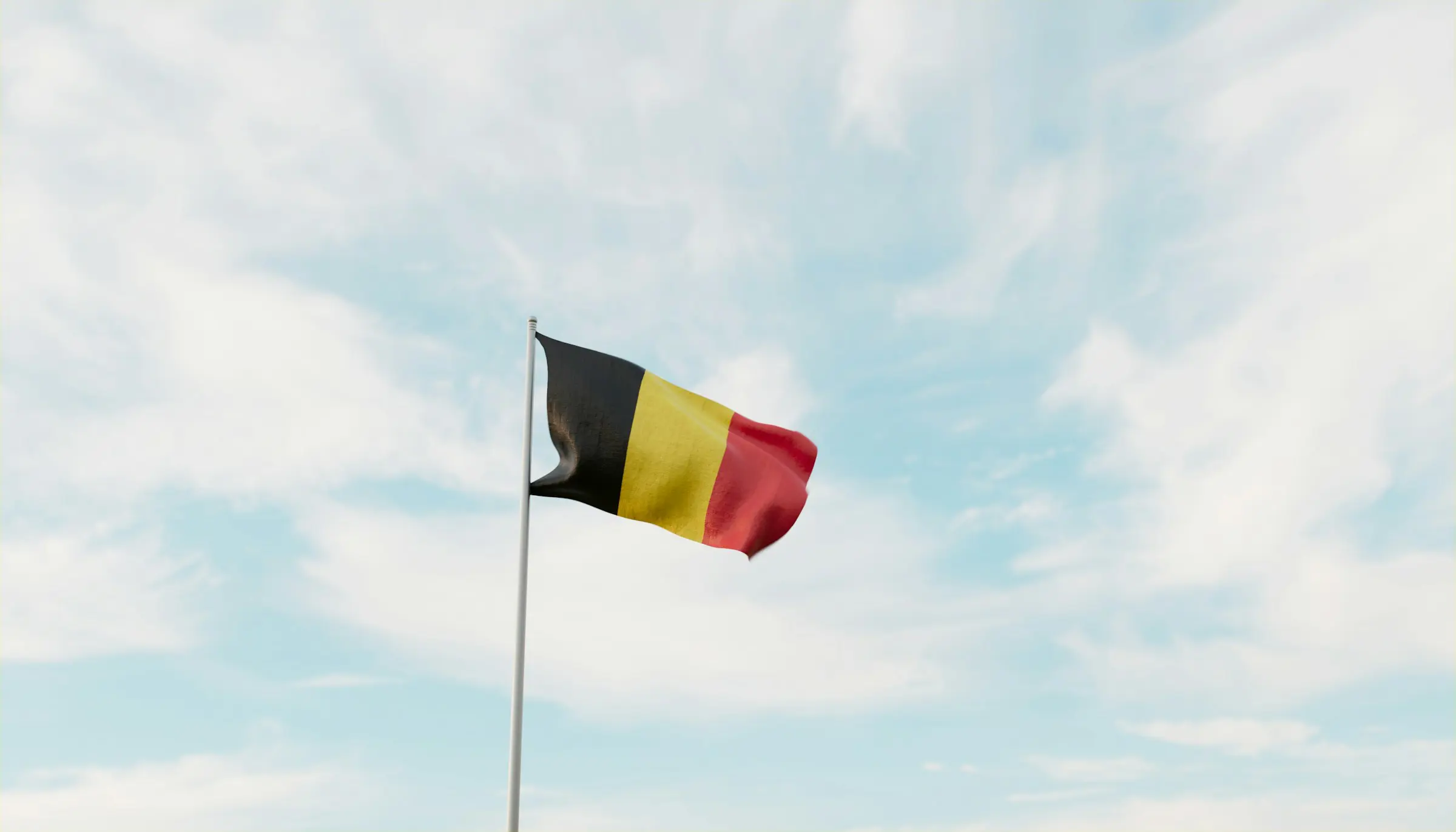 Belgisk flagga vajar mot blå himmel med lätta moln