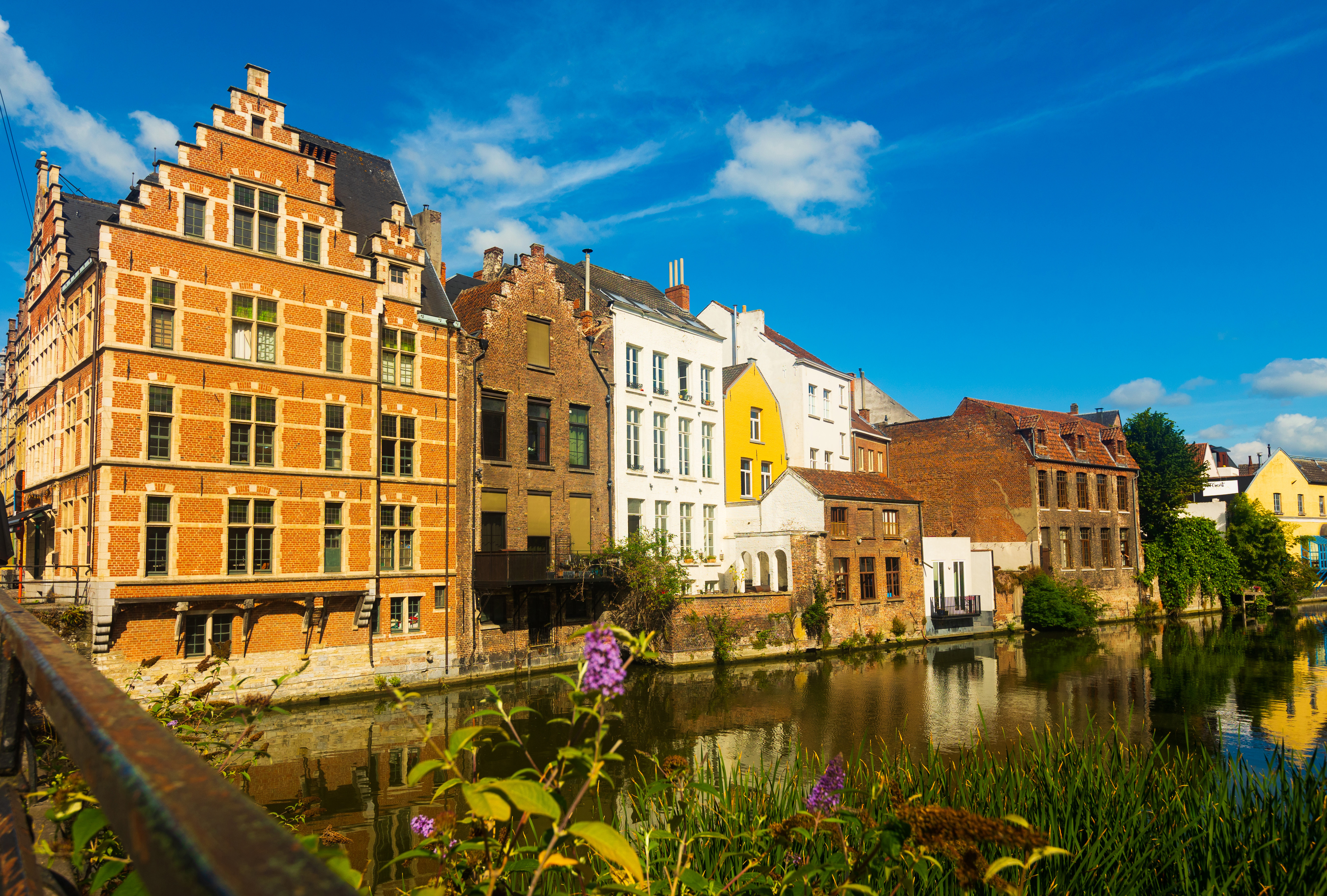 Travel to Belgium - Historic buildings along a canal in Ghent, Belgium, with colorful facades reflecting in the water.