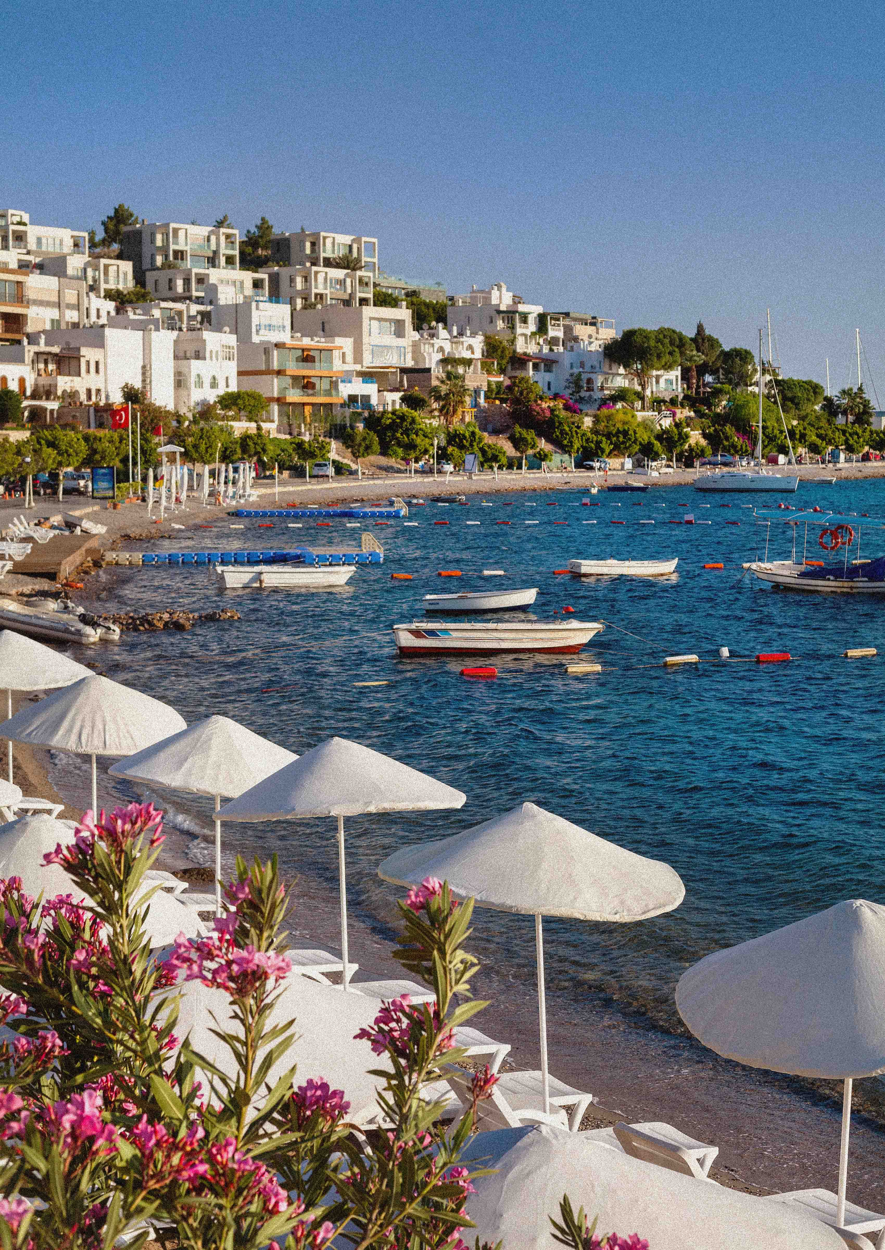 Beach in Bodrum with white umbrellas, clear water and hotels on the coast of Turkey