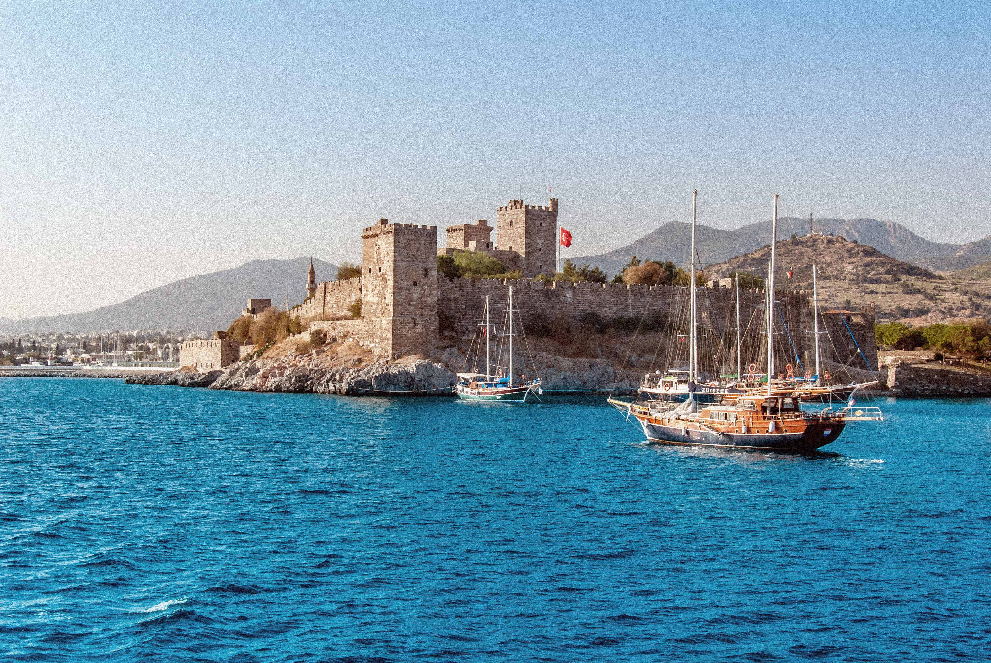 Bodrums slott vid havet med segelbåtar i förgrunden och berg i bakgrunden i Turkiet