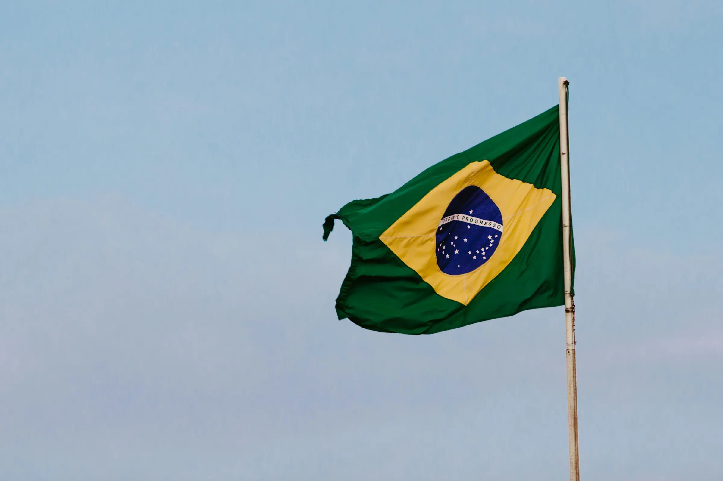Brazilian flag waving on a pole against a clear blue sky.
