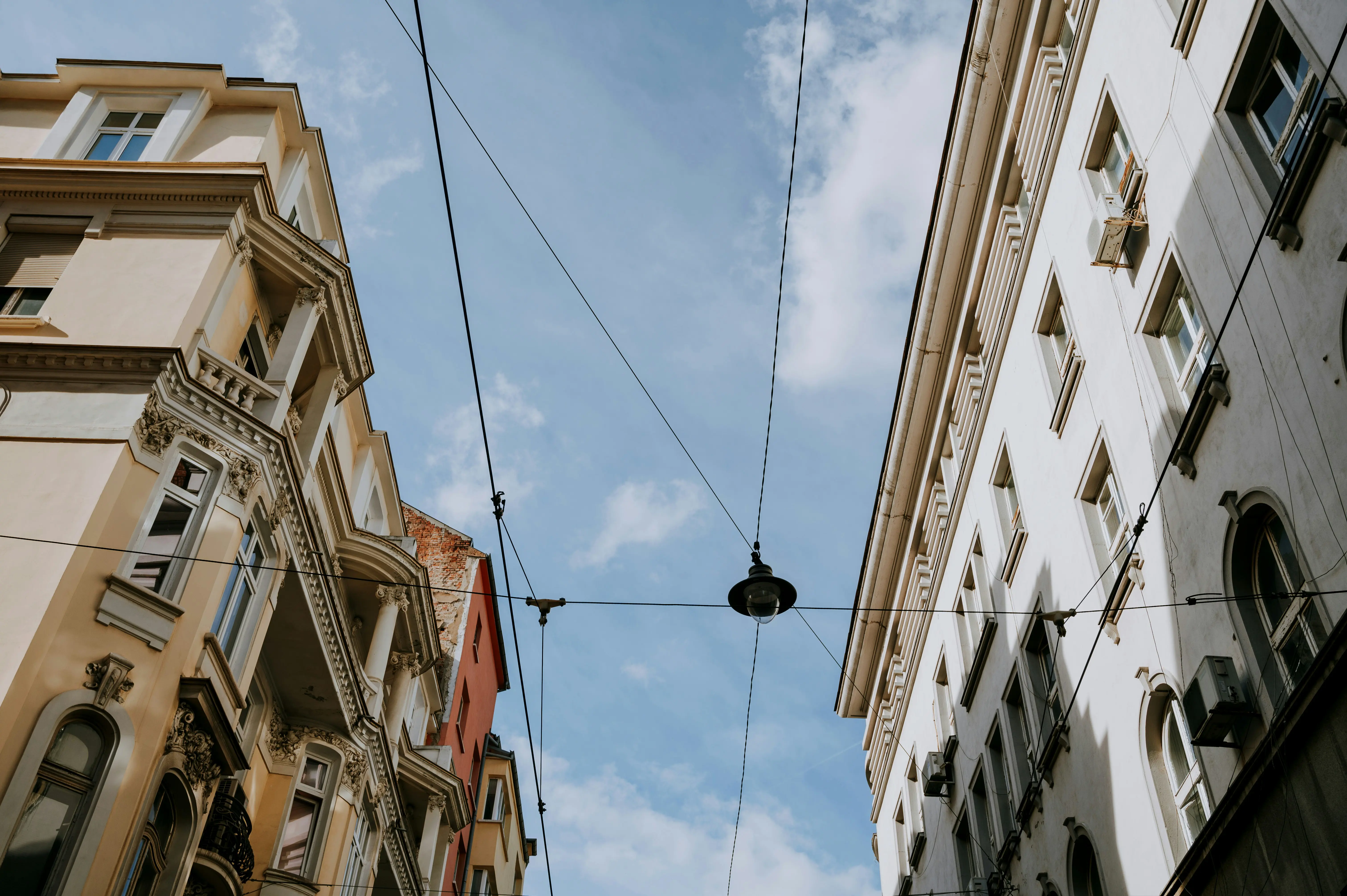 Street with historic European architecture buildings and overhead wires against a blue sky.