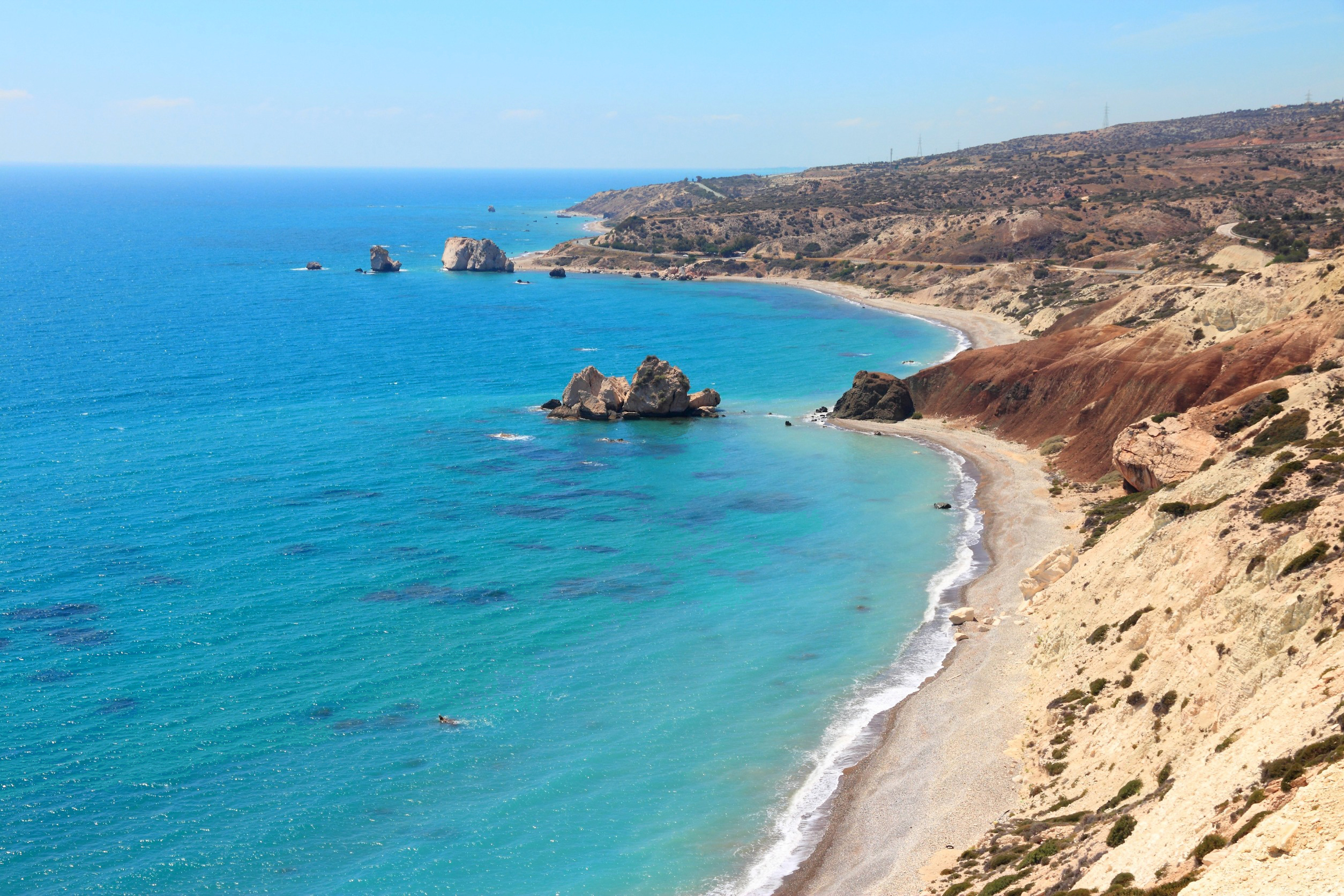 Travel to Cyprus - Scenic view of Petra tou Romiou beach featuring turquoise waters, rocky coastline, and clear blue sky.
