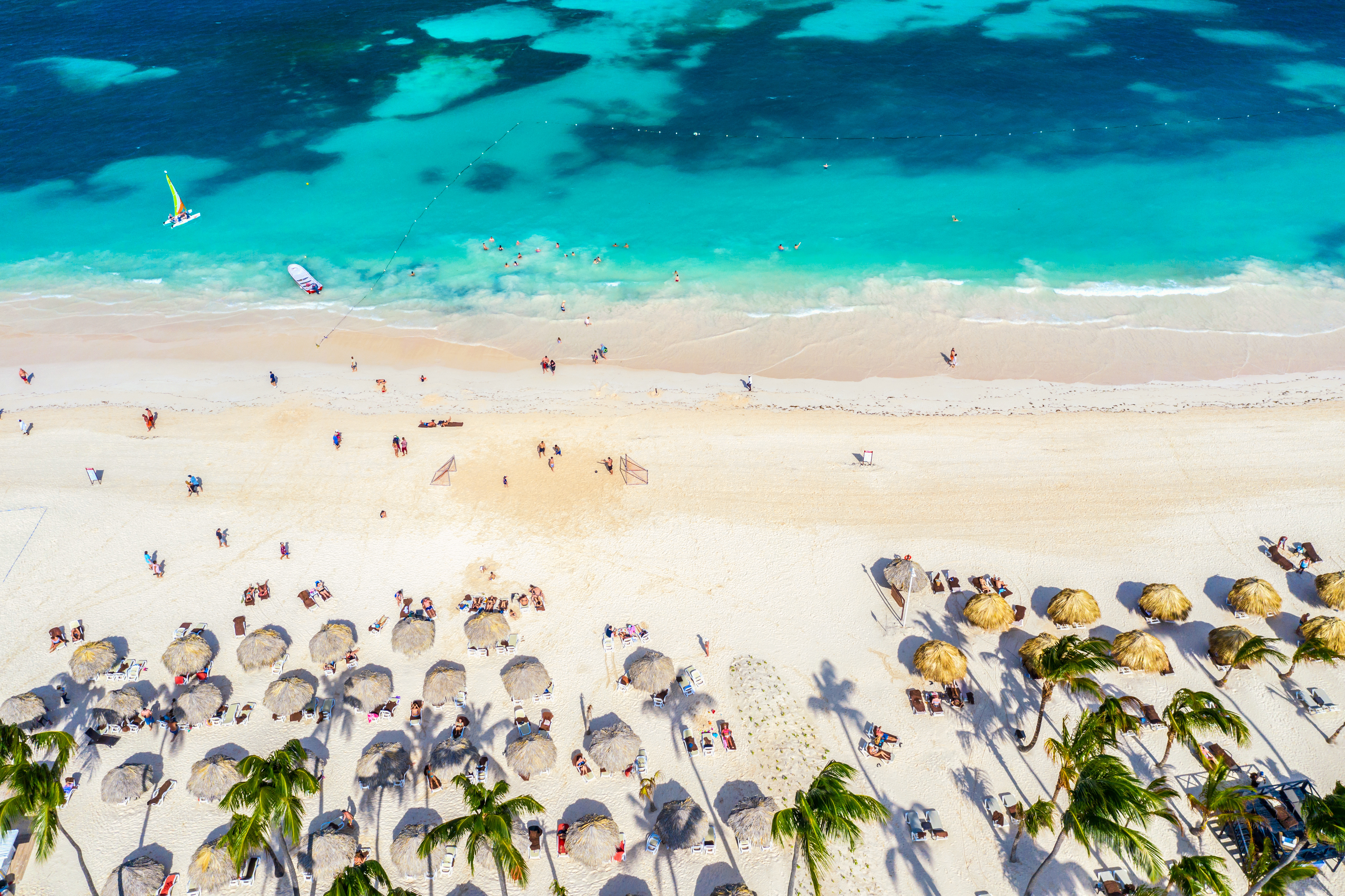 Travel to Dominican Republic - view of a tropical beach with turquoise waters, white sand, palm trees, and beachgoers relaxing
