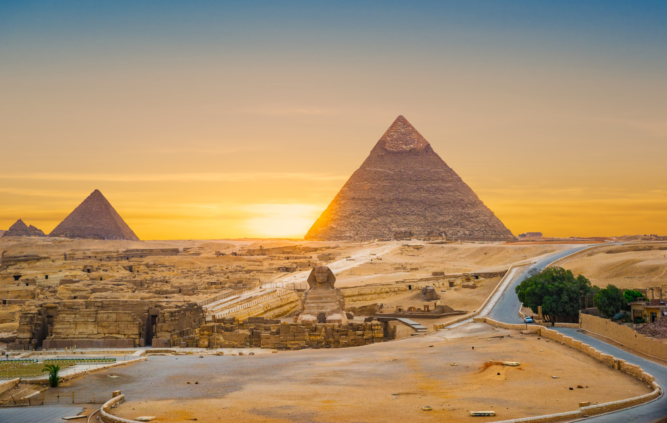 Travel to Egypt - view of the Pyramids of Giza and the Sphinx in Egypt, with a vibrant orange sky illuminating the historic desert landscape.