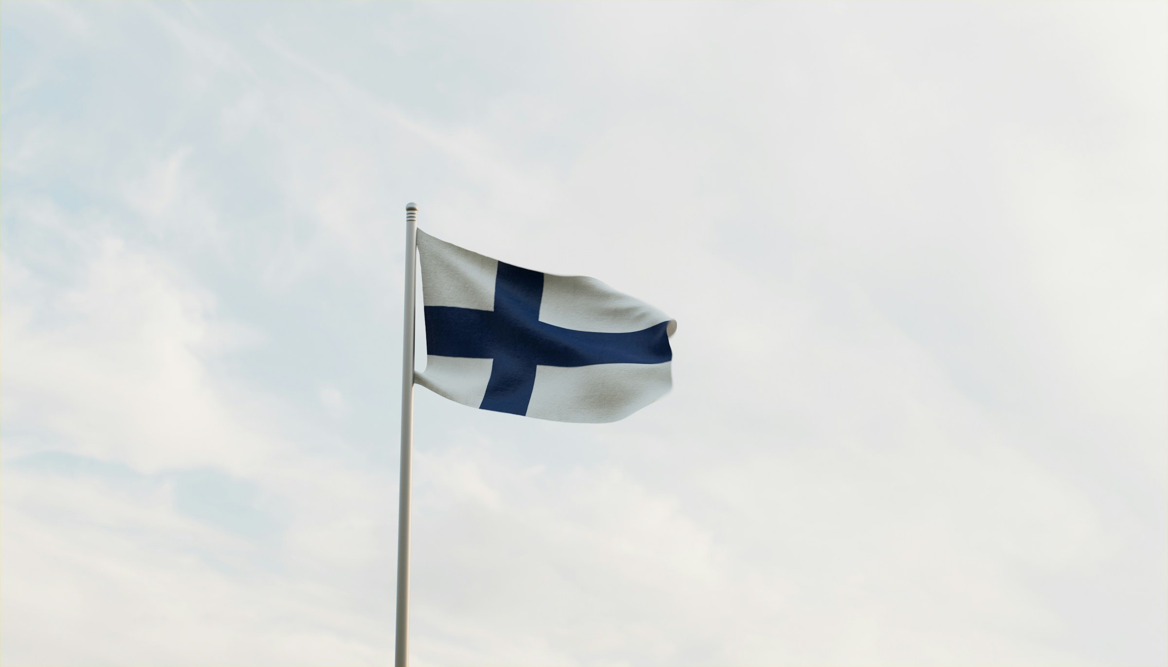 Finnish flag with a blue cross on a white background waving against a cloudy sky.
