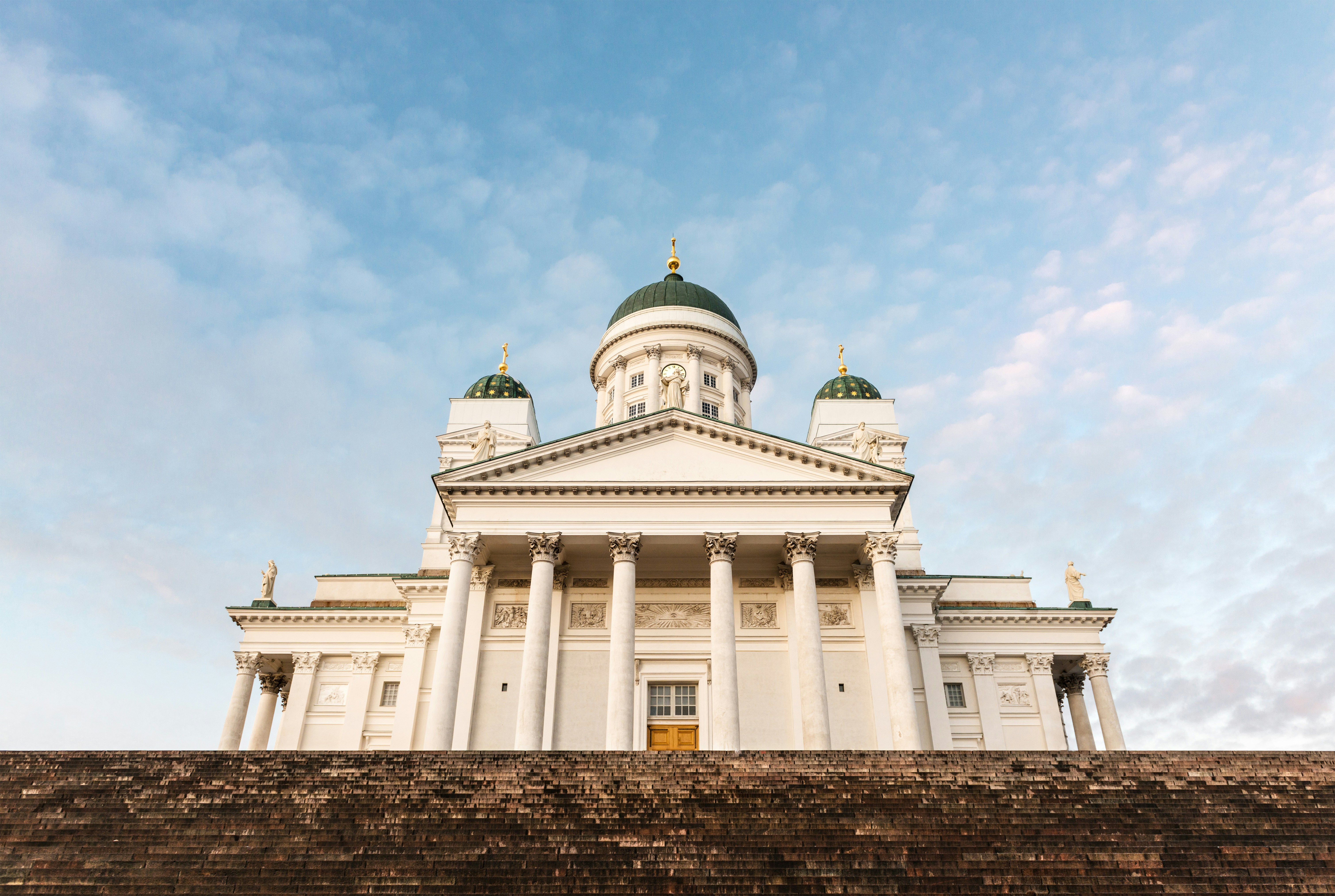 Helsinki Cathedral against a clear blue sky, featuring neoclassical architecture with white columns and green domes.