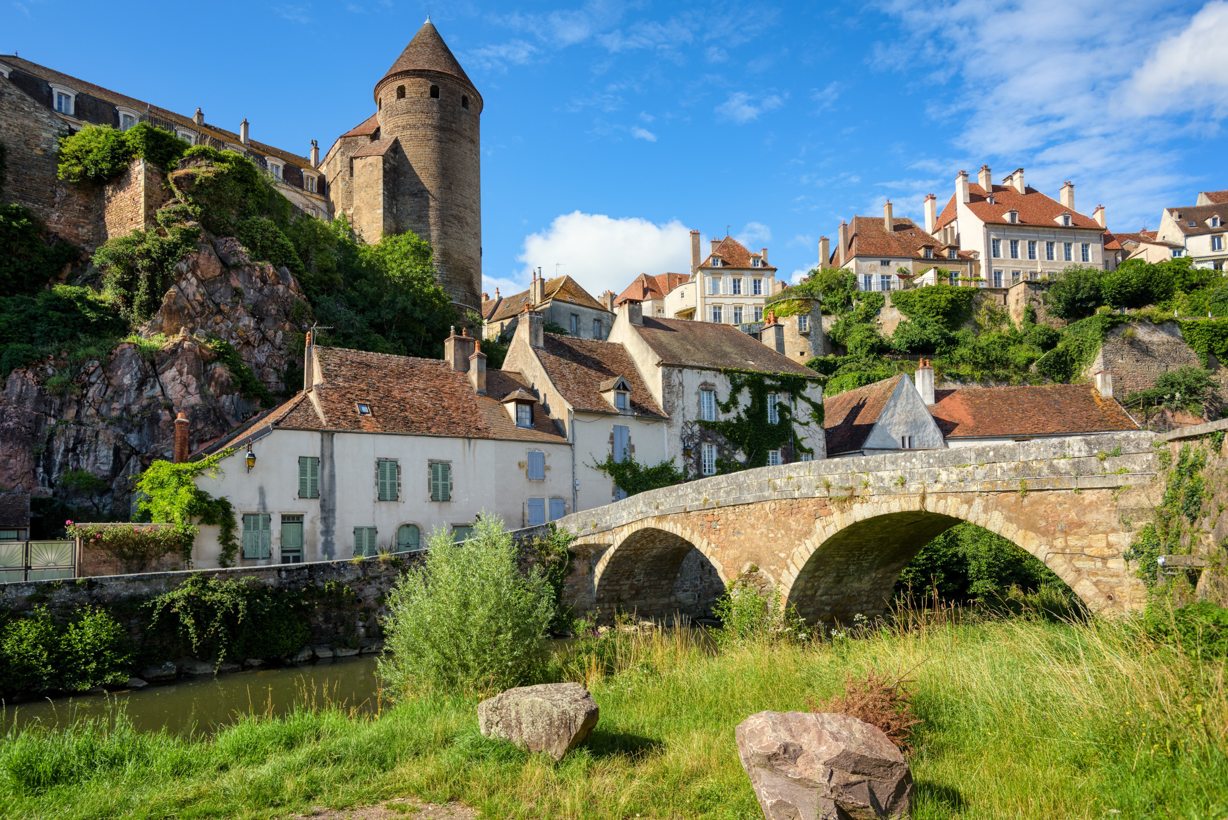 Travel to France - stone bridge and picturesque village of Semur-en-Auxois in Burgundy with historic towers and traditional houses under a blue sky.