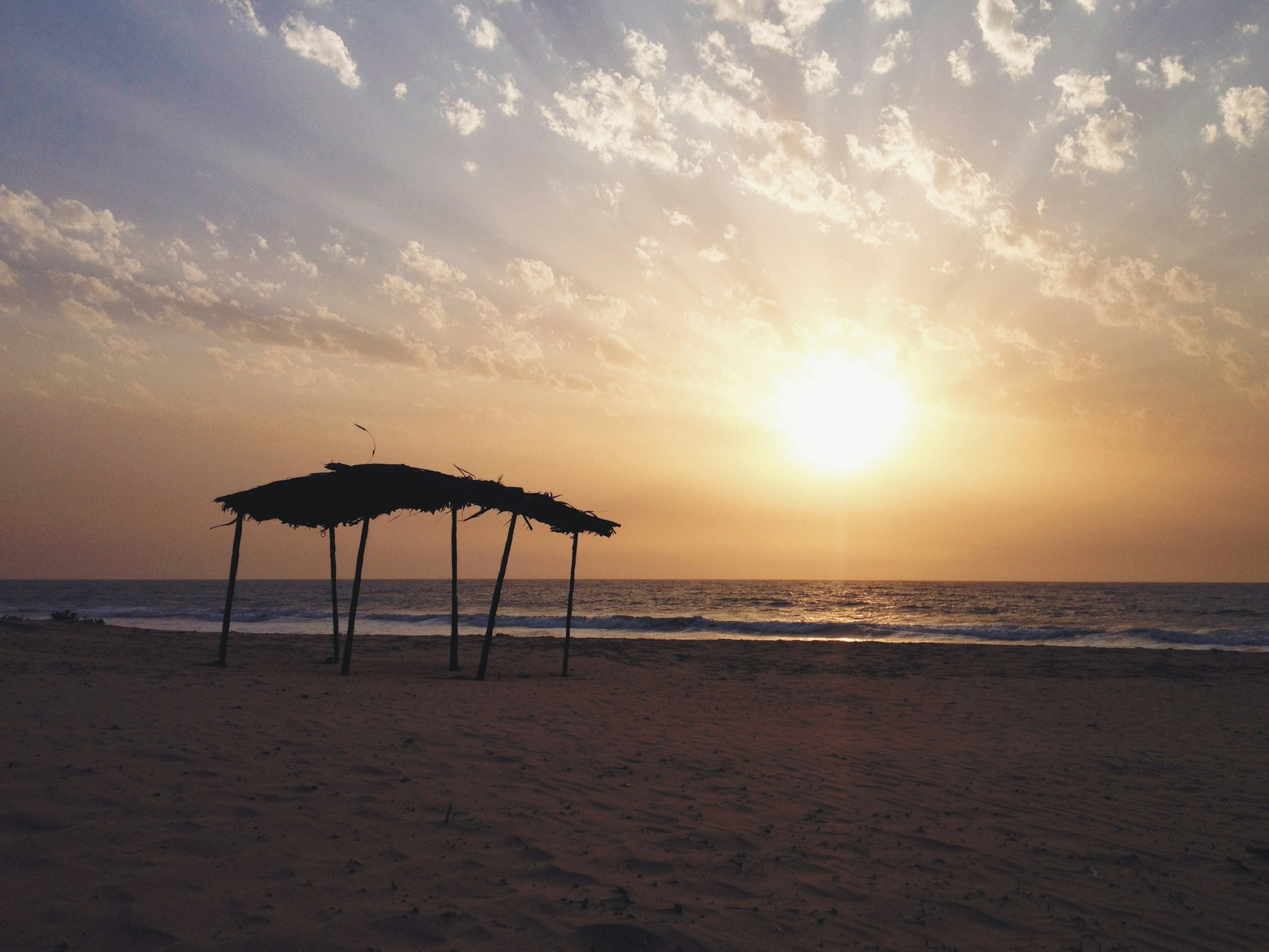 Sunset over a tranquil beach with a rustic wooden canopy in the foreground, capturing the serene coastal landscape.