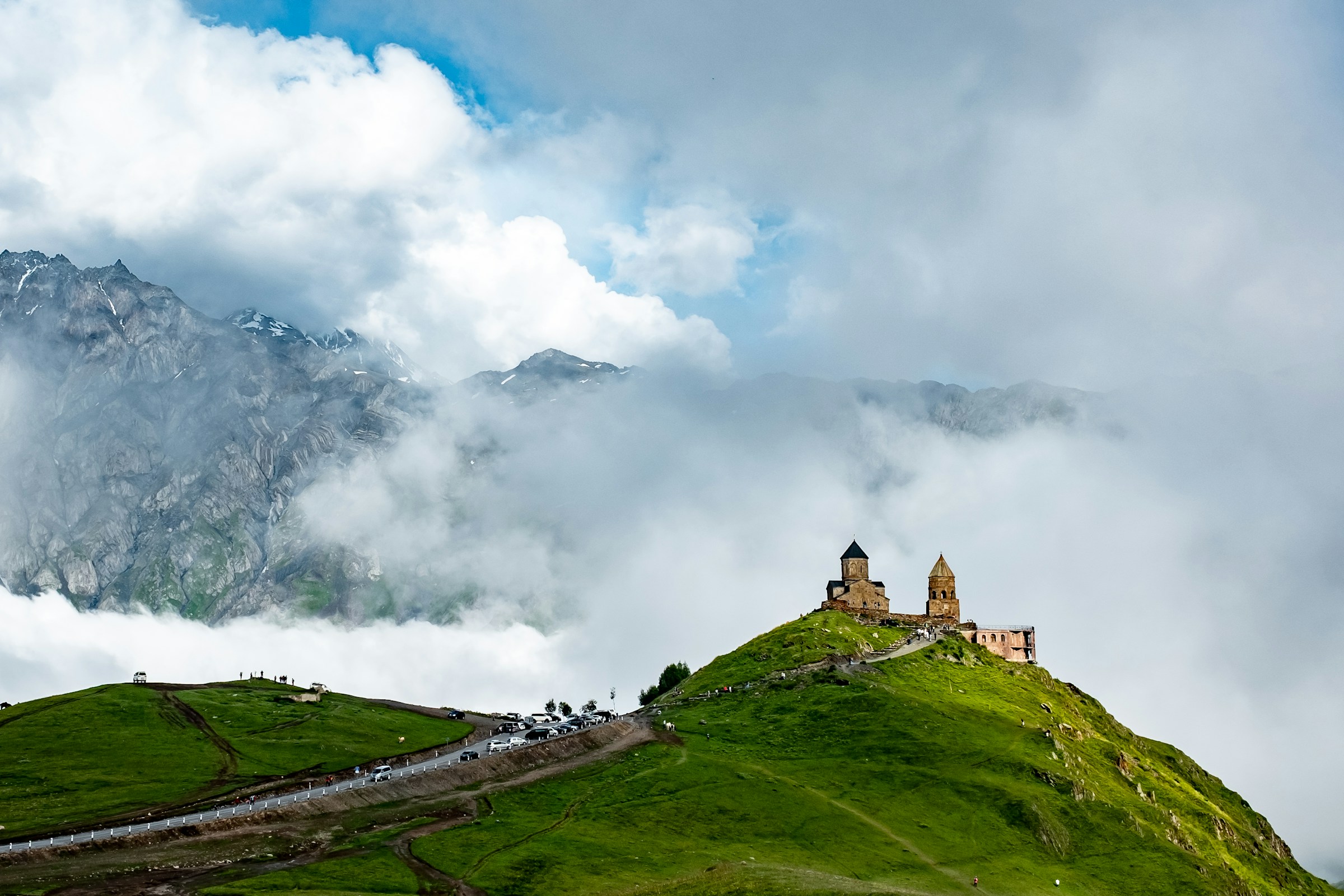 Kyrka på bergstopp omgiven av grönskande landskap och dimhöljda berg i bakgrunden i Georgien.