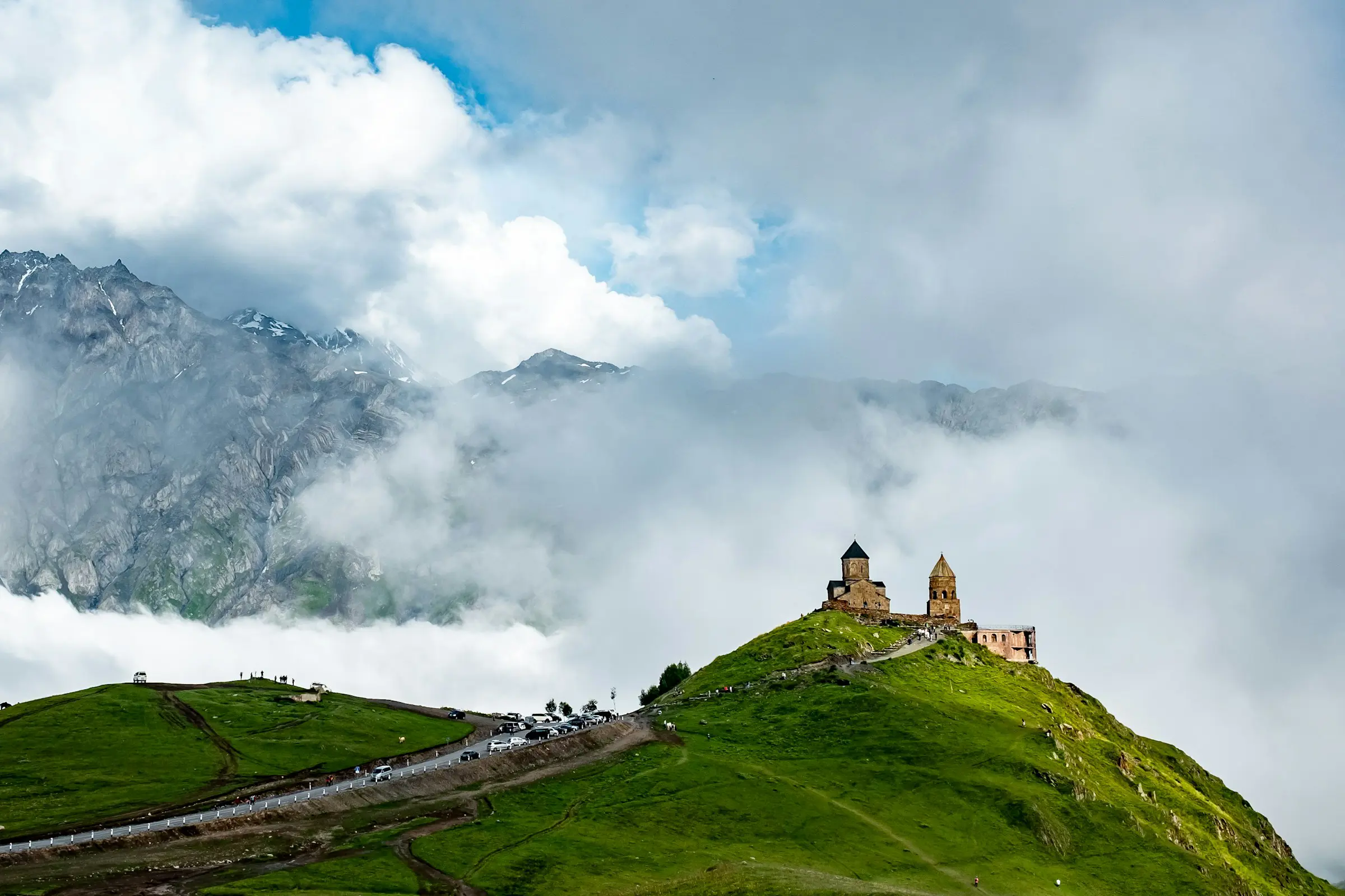 Kyrka på bergstopp omgiven av grönskande landskap och dimhöljda berg i bakgrunden i Georgien.