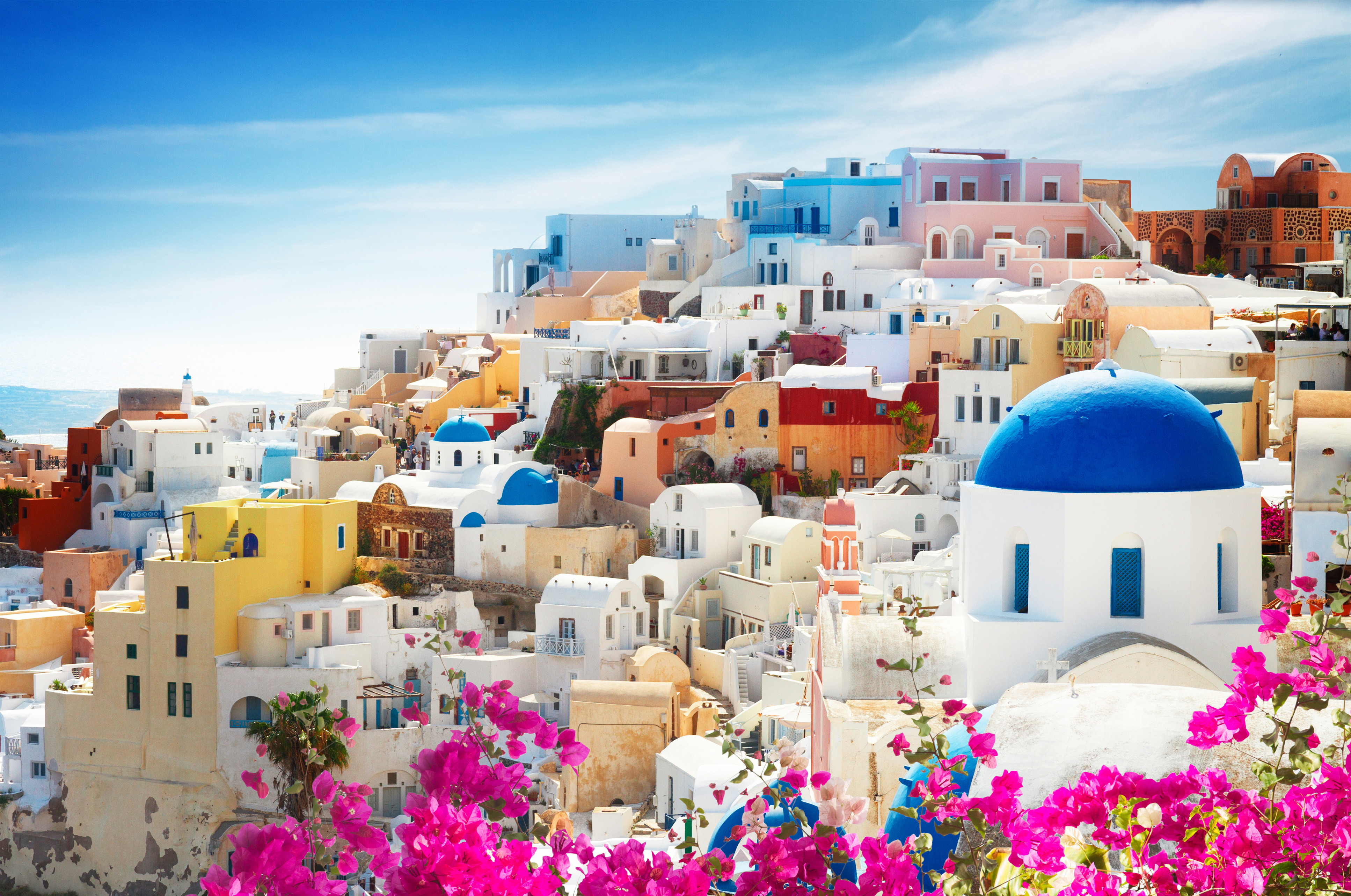 Travel to Greece - Colorful buildings with blue domed rooftops in Greece, under a clear sky, framed by vibrant pink flowers.