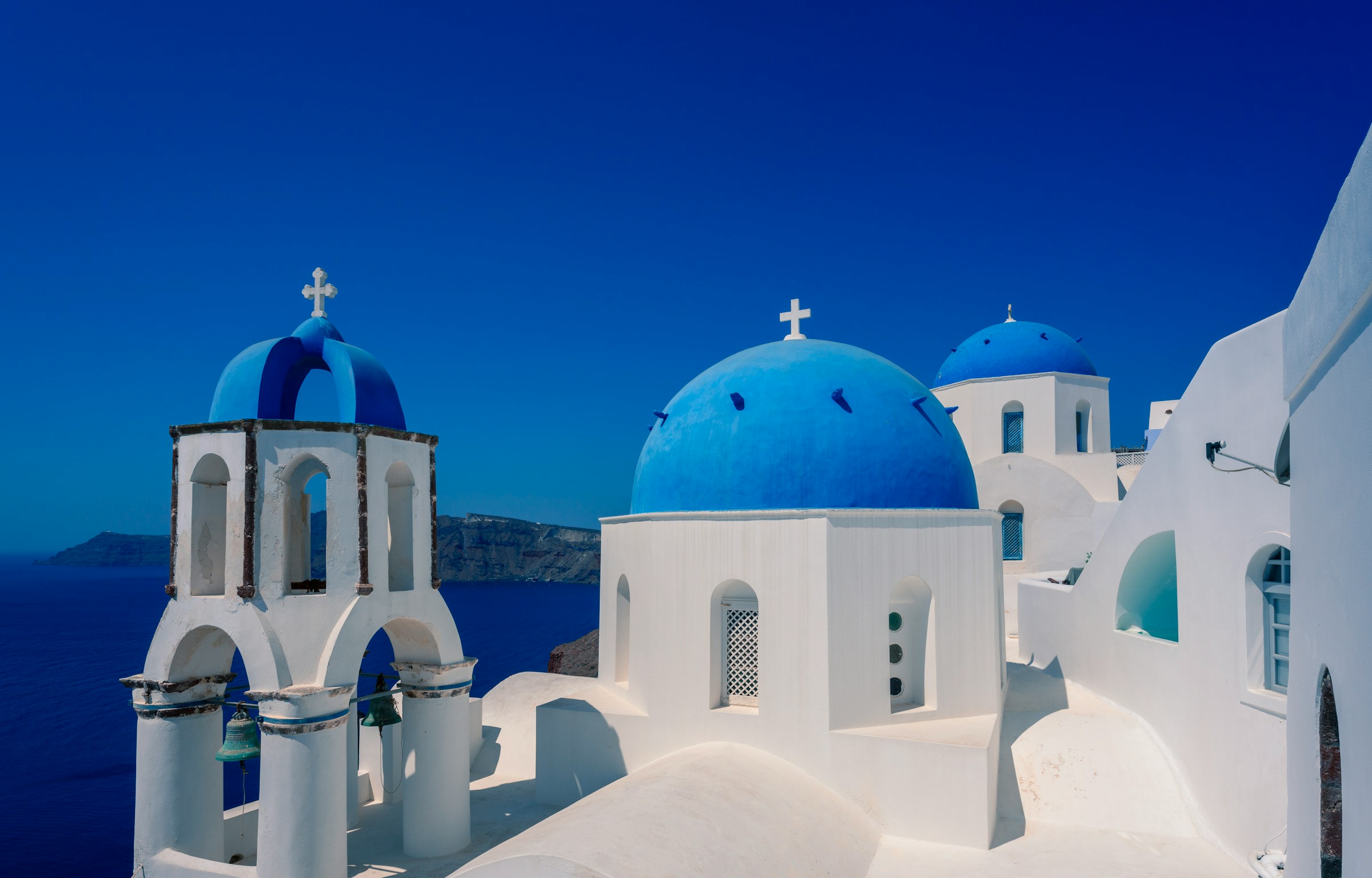 White buildings with blue domes in Santorini, Greece, overlooking a clear blue sea.