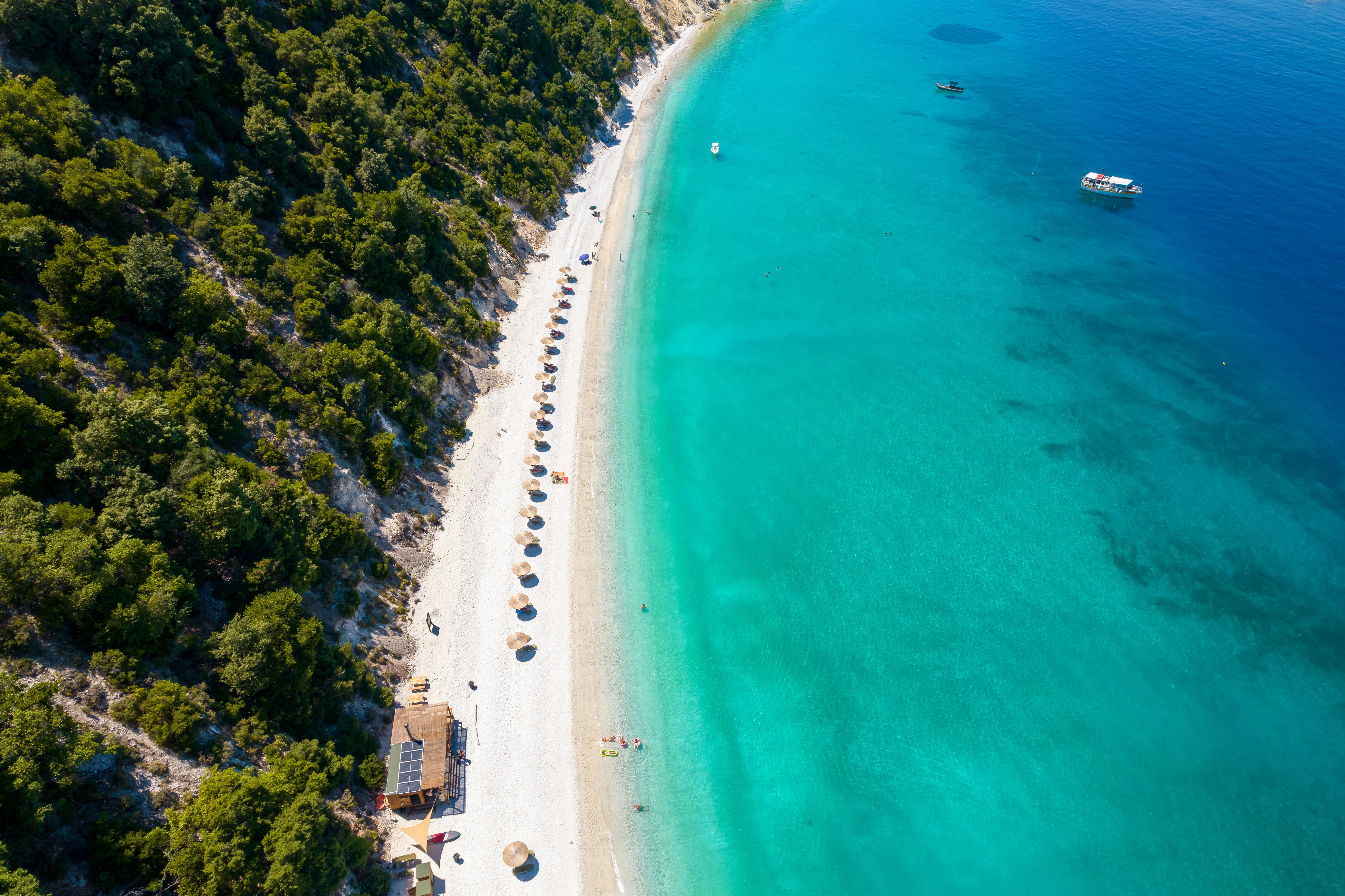 Travel to Thassos - view of a picturesque beach with turquoise waters, lined with umbrellas and sun loungers, bordered by lush green trees.