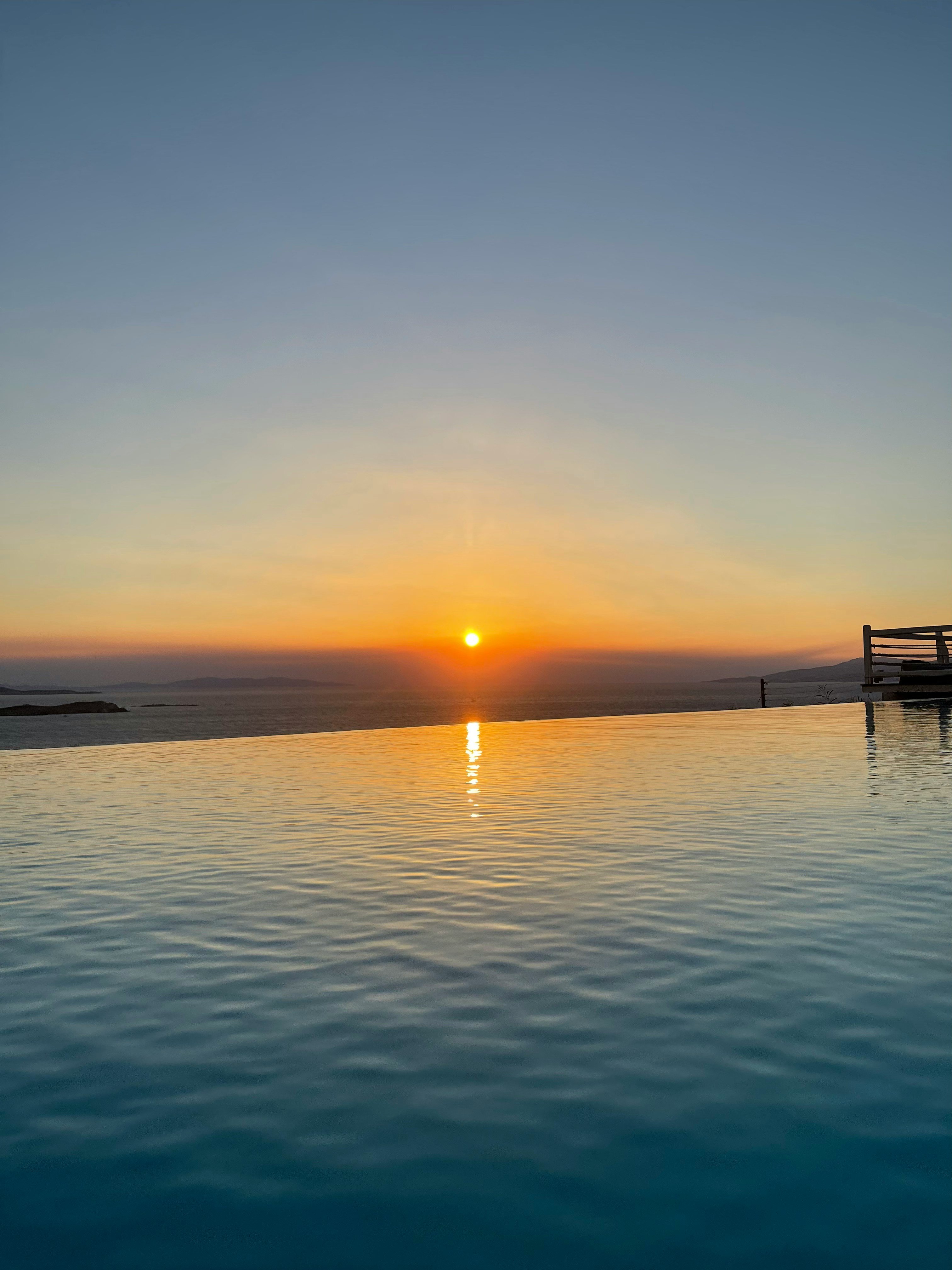 Sunset view over an infinity pool with a calm ocean horizon in the distance, creating a serene and picturesque scene.