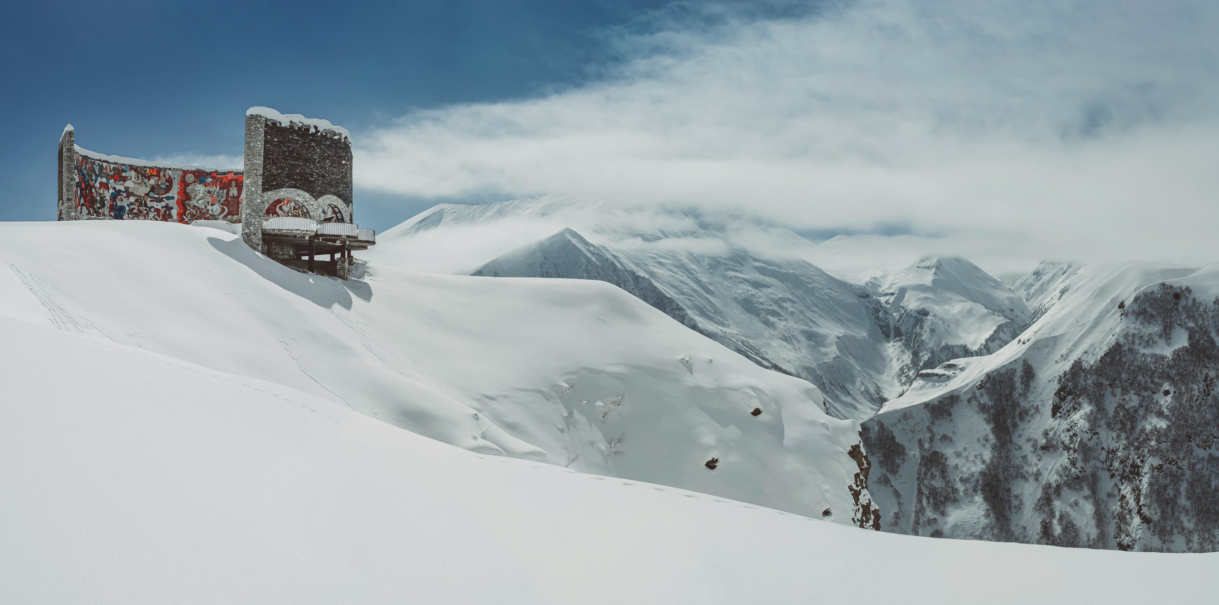 Snow-covered mountain landscape with colorful ornate building and cloudy sky in the background, beautiful and distant winter landscape.