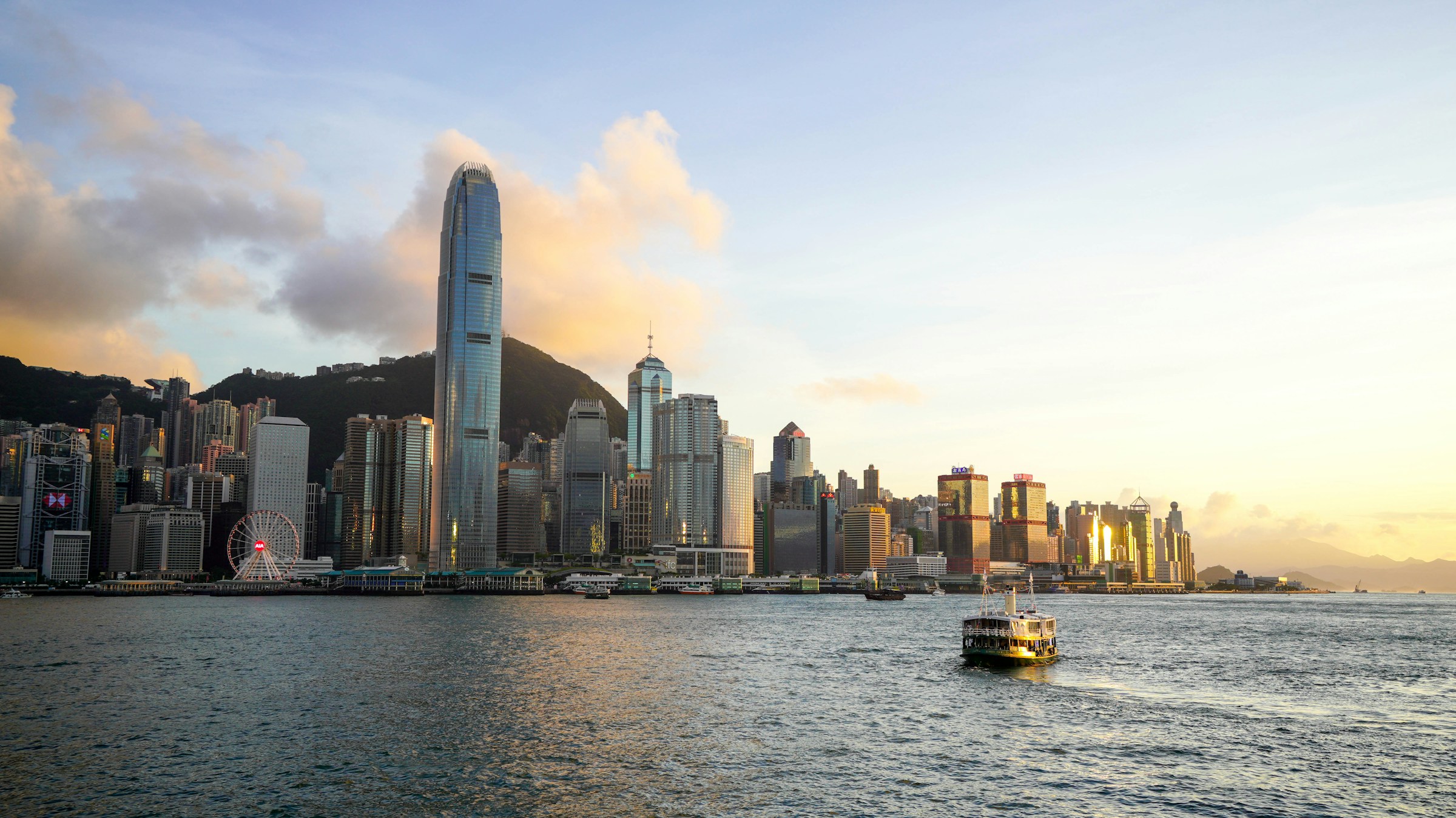 Hong Kong skyline at sunset with Victoria Harbour and ferry in the foreground.