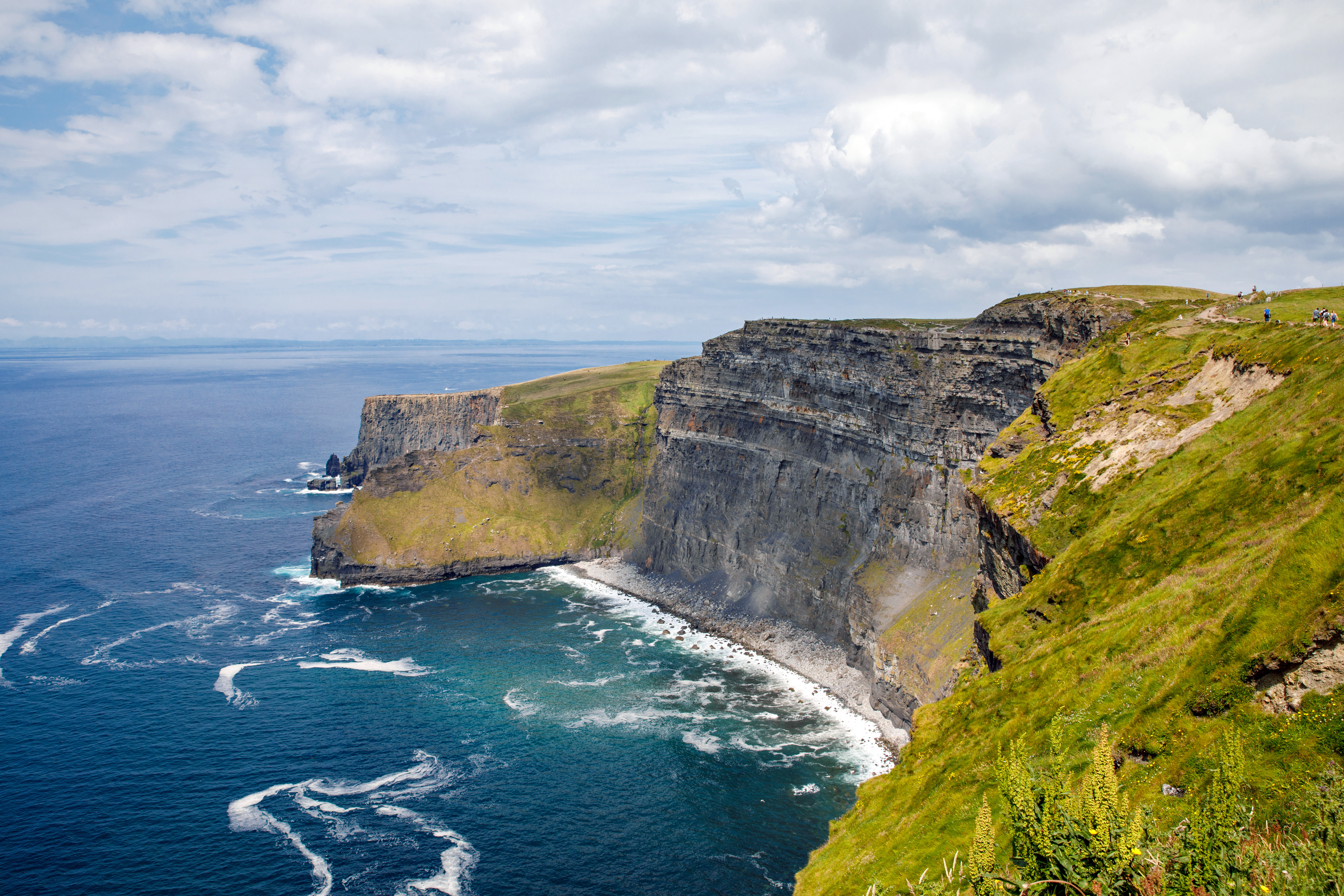 Travel to Ireland - Cliffs of Moher with ocean waves crashing below, showcasing rocky cliffs and green landscapes.