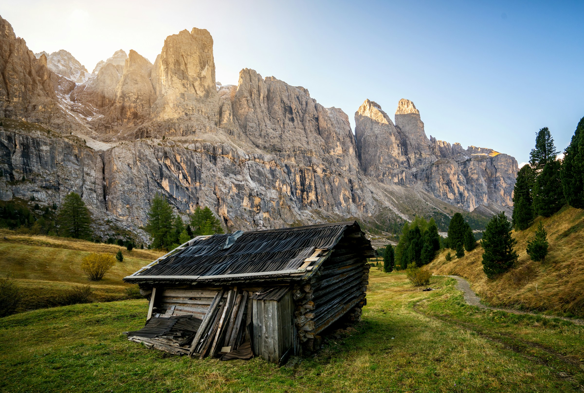 En ensam stuga står i en grön dal mellan mäktiga klippor i Val Gardena men en soluppgång i bakgrunden