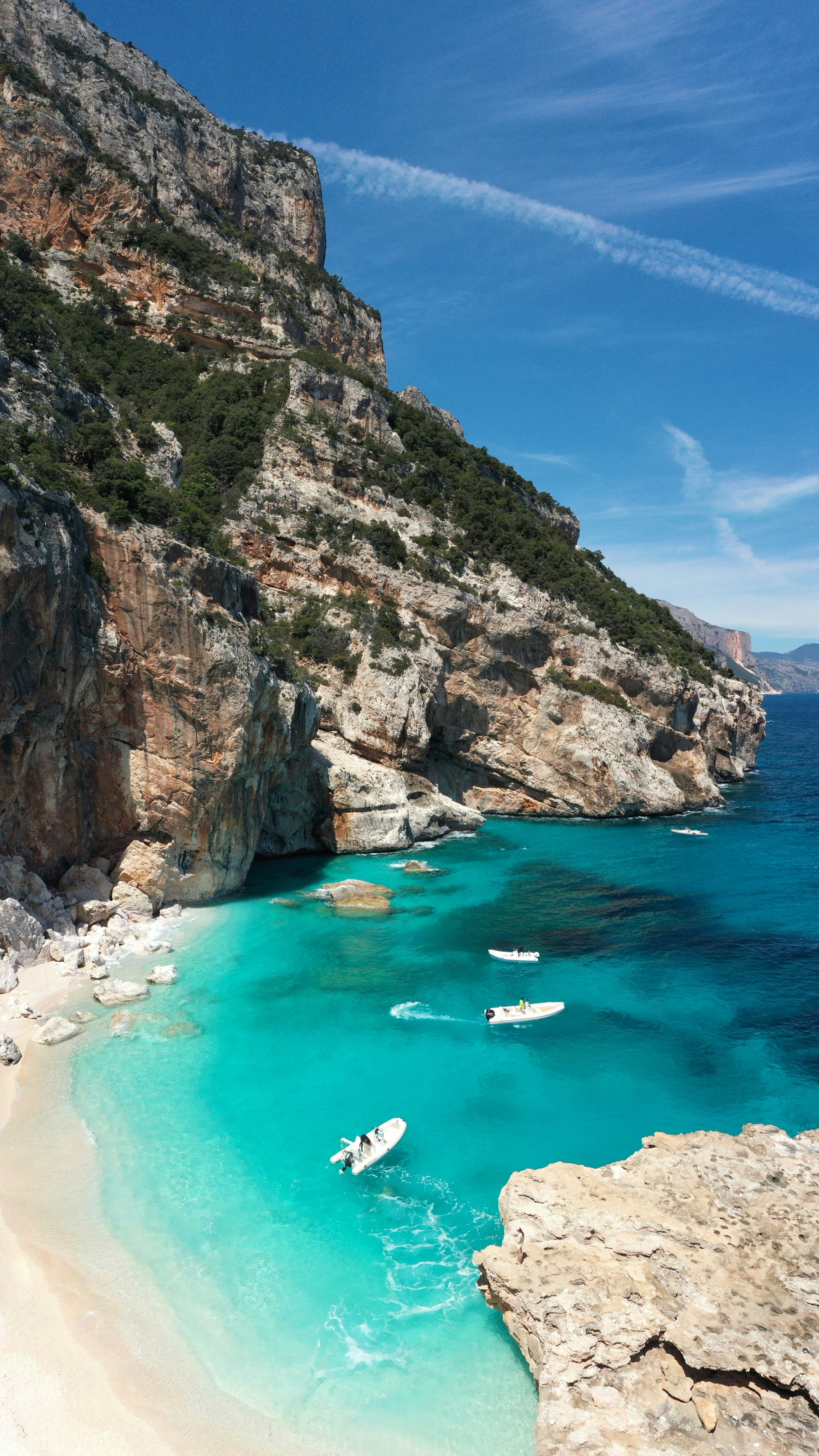 Scenic view of a turquoise bay with small boats near rocky cliffs, under a clear blue sky.