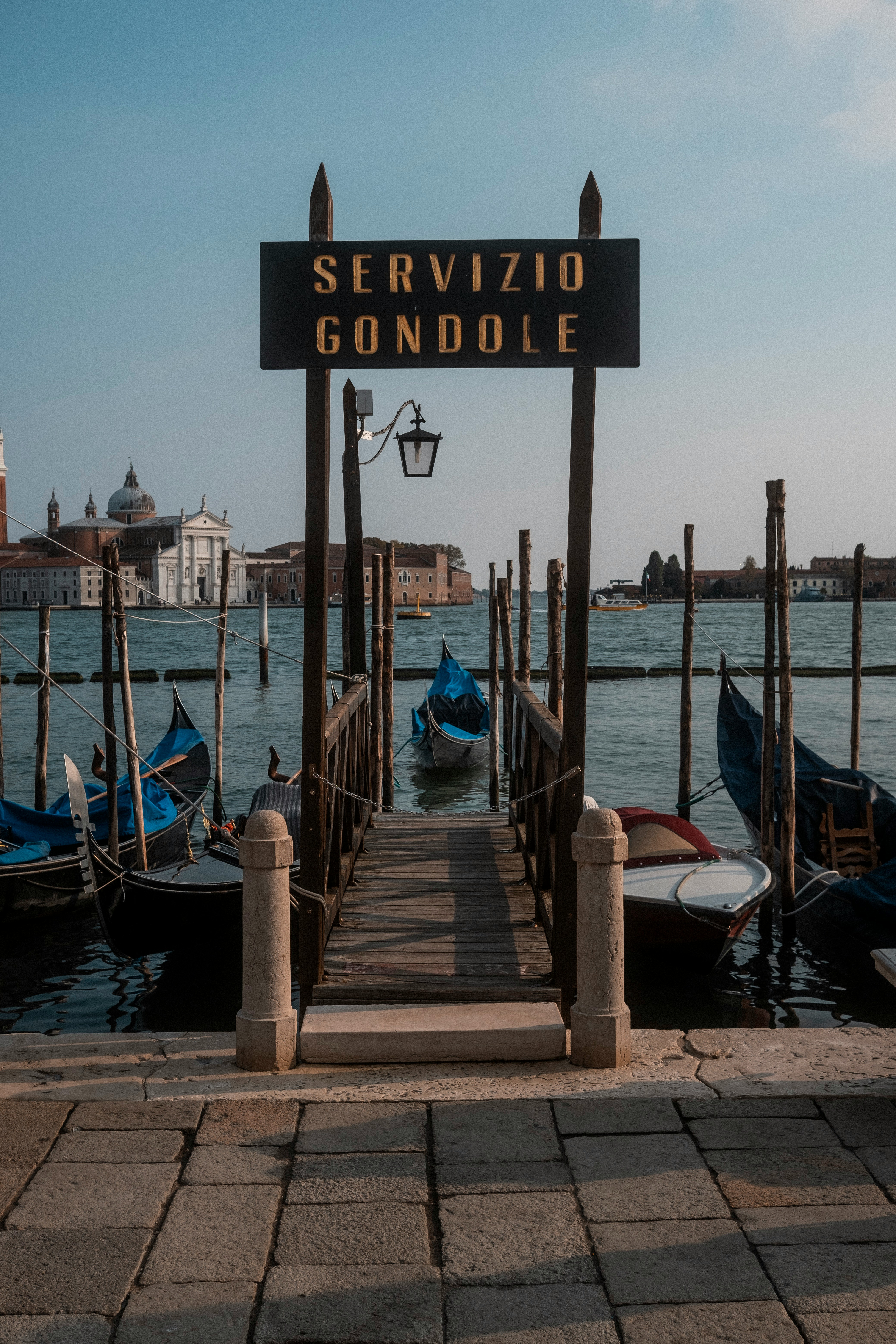Brygga för gondoltjänster i Venedig med flera gondoler, omgiven av vatten och historiska byggnader i bakgrunden