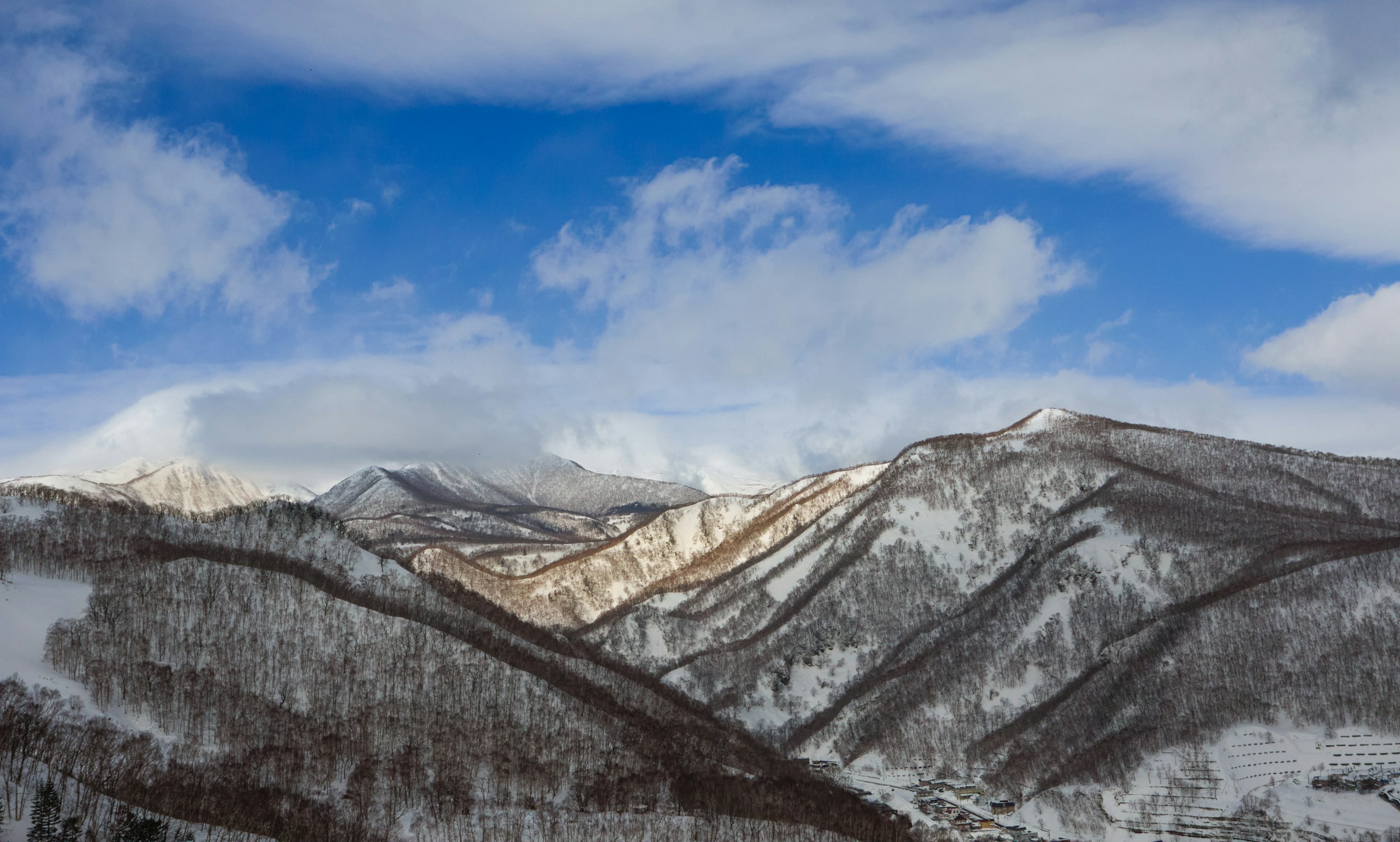 Snow-capped mountains under a clear blue sky with clouds in Hokkaido, Japan.